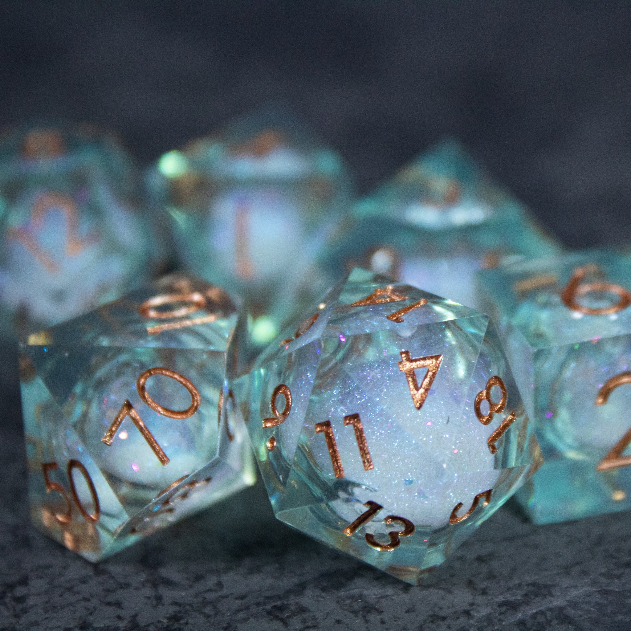Will o' Wisp Liquid Core Dice Set - Translucent blue-green liquid core polyhedral dice set with sharp edges and copper-colored numbers.