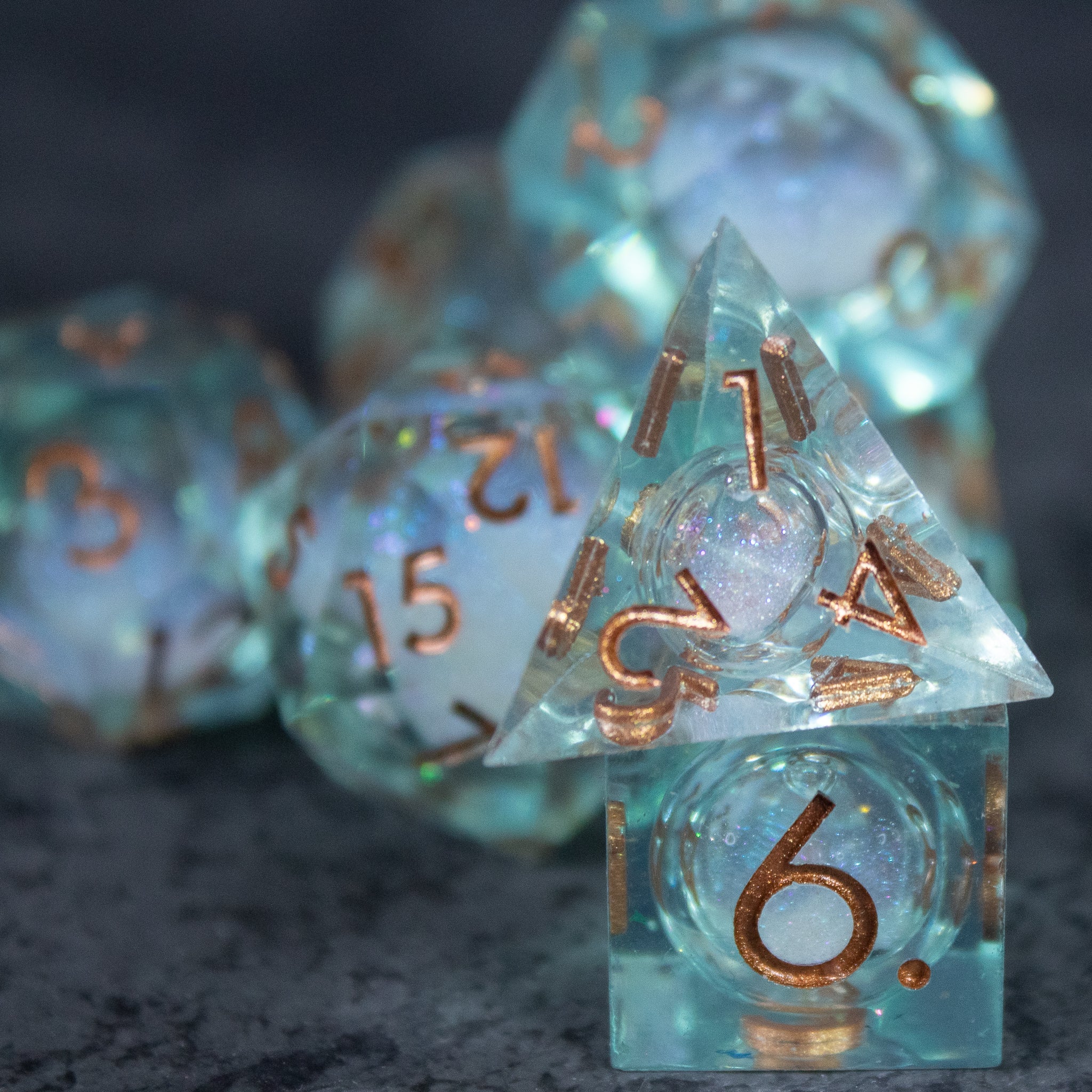 Will o' Wisp Liquid Core Dice Set - Set of translucent aqua liquid core polyhedral dice with sharp edges and metallic bronze numbers.