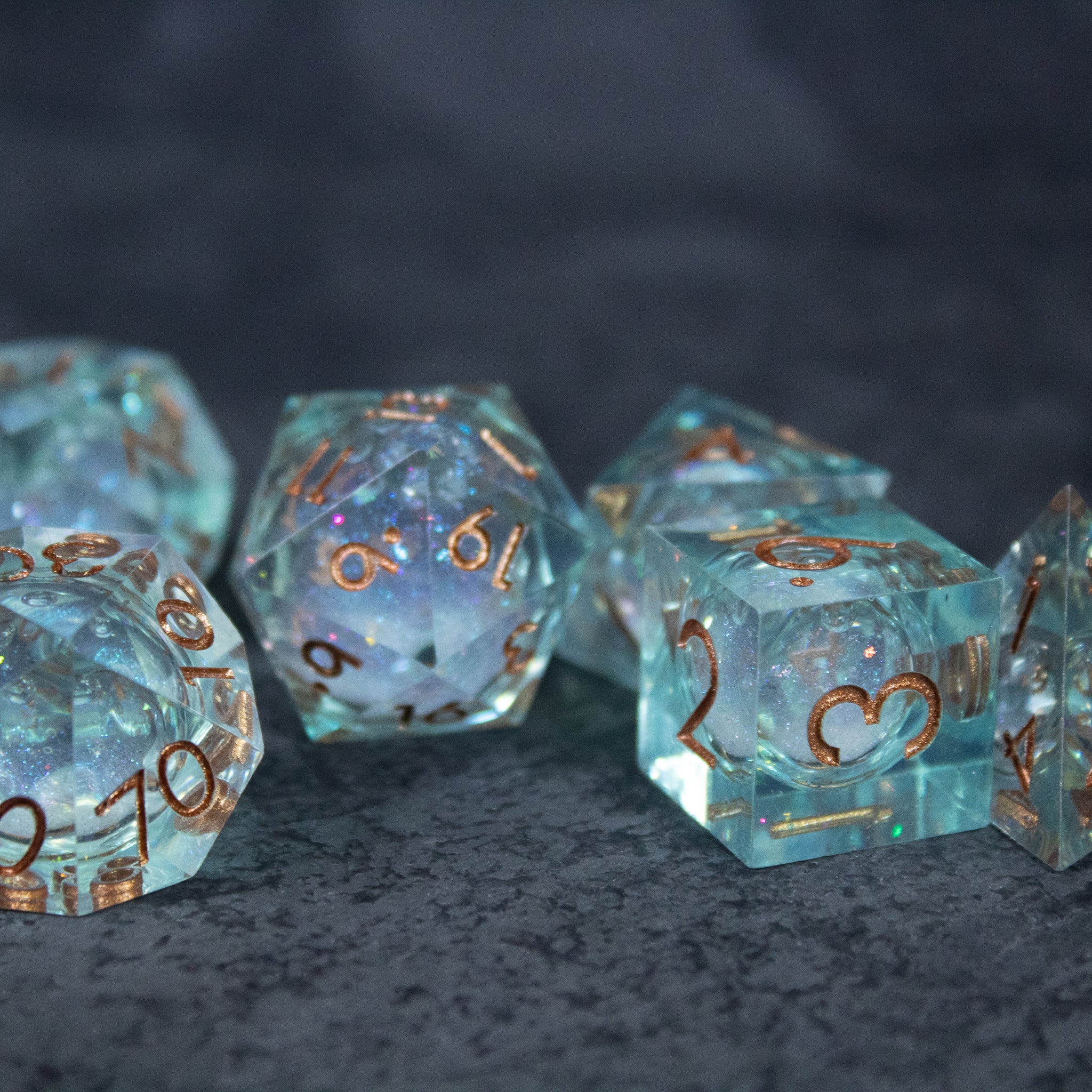 Will o' Wisp Liquid Core Dice Set - Set of translucent light blue polyhedral dice with gold flakes and sharp edges, featuring gold numbered inscriptions.