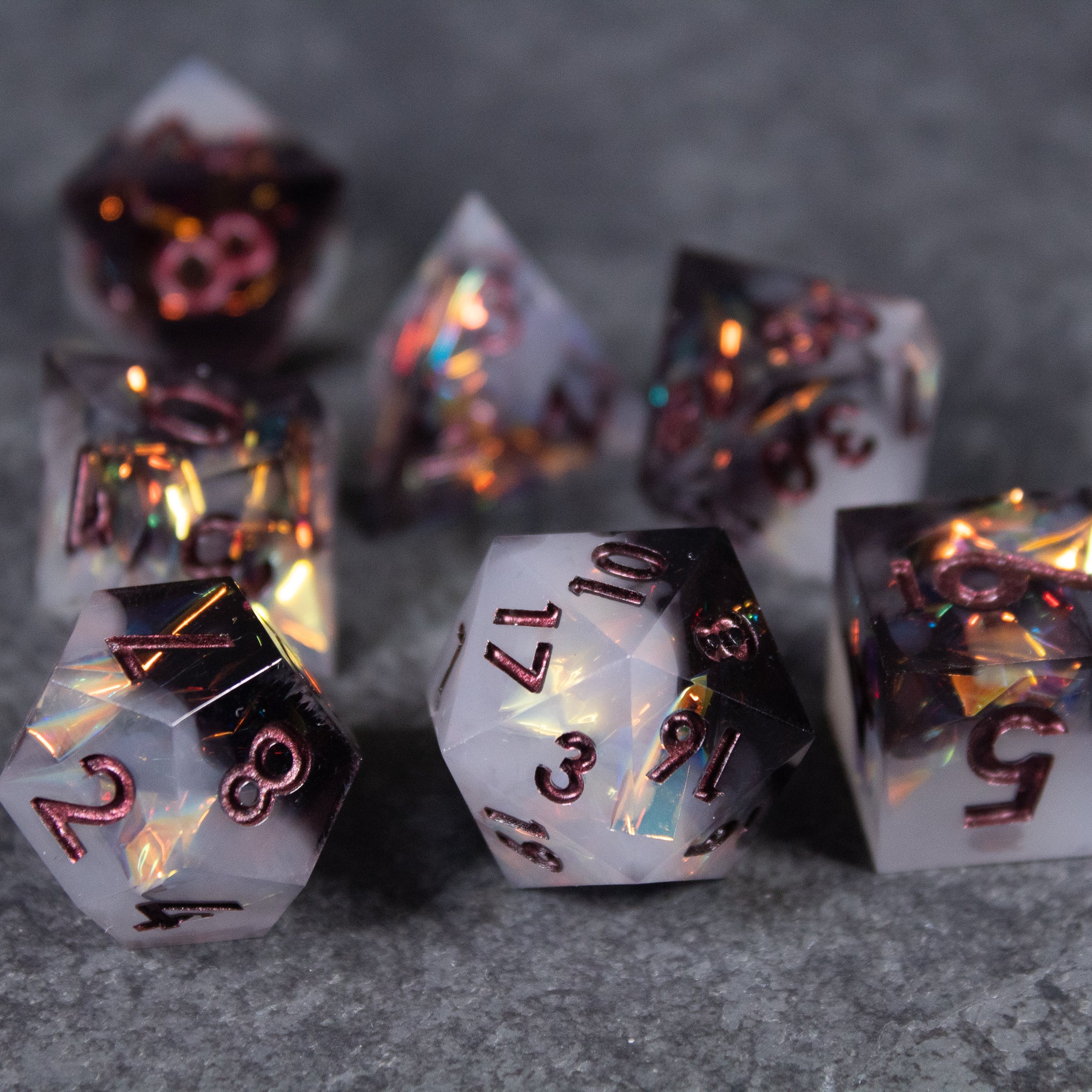 Oathbreaker Dice Set - Seven black and white sharp-edged polyhedral dice with iridescent orange-gold flecks and metallic numbers.
