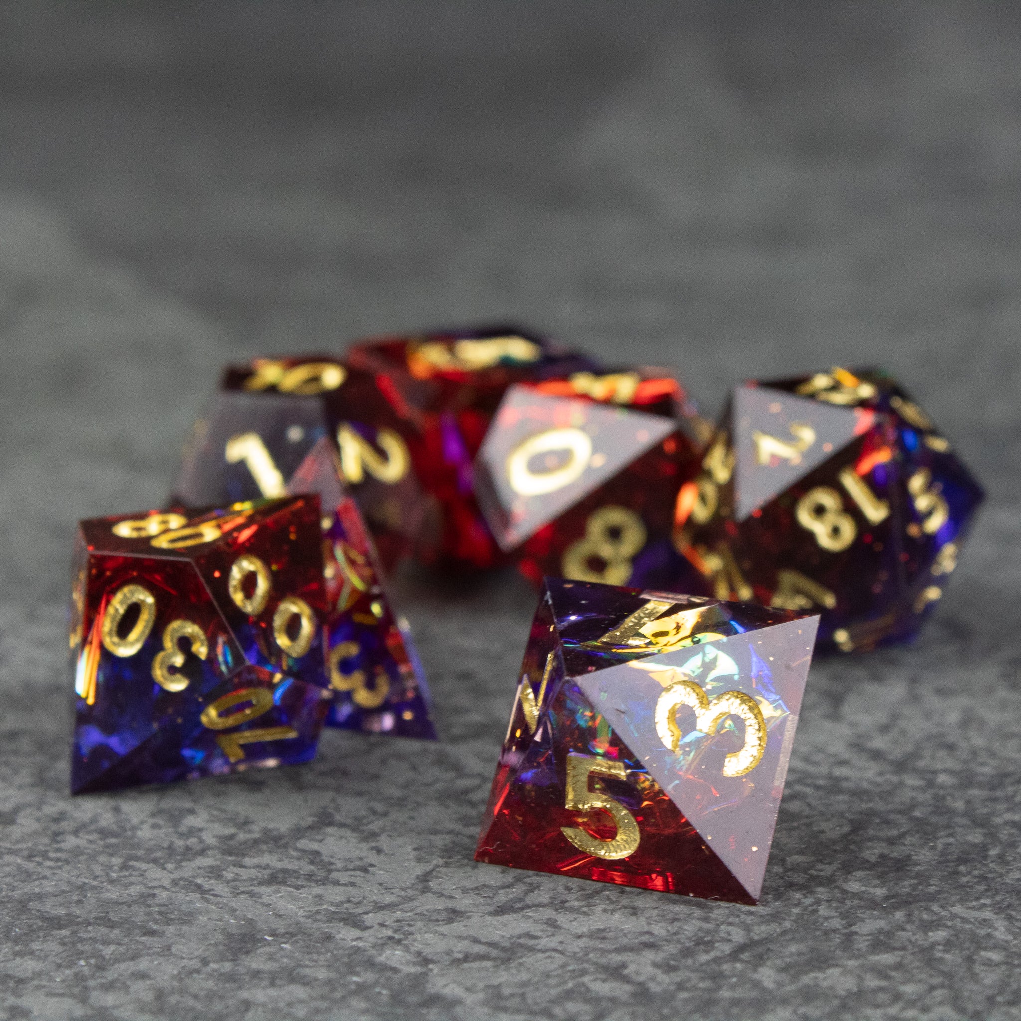Electromancer Dice Set - Sharp-edged polyhedral dice set in blue and red with gold numbering on a gray surface.