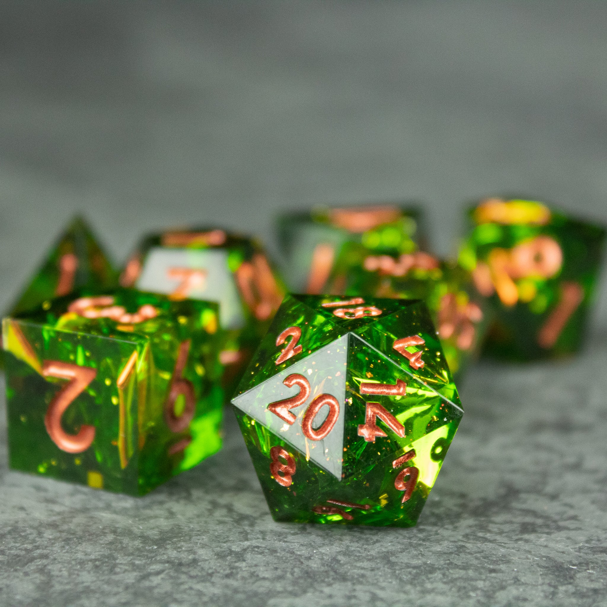 Venom Dice Set - Green translucent sharp-edged 20-sided dice with copper metallic numbers on gray surface.