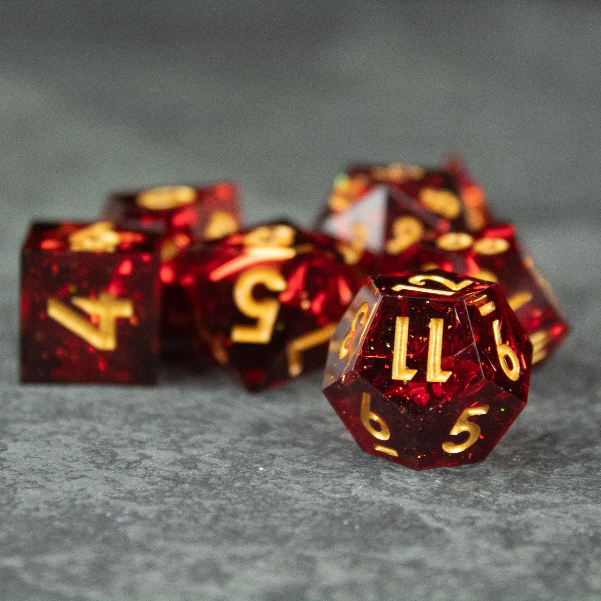 Ember Dice Set - Red translucent sharp-edged polyhedral dice set with gold numbering on gray surface.