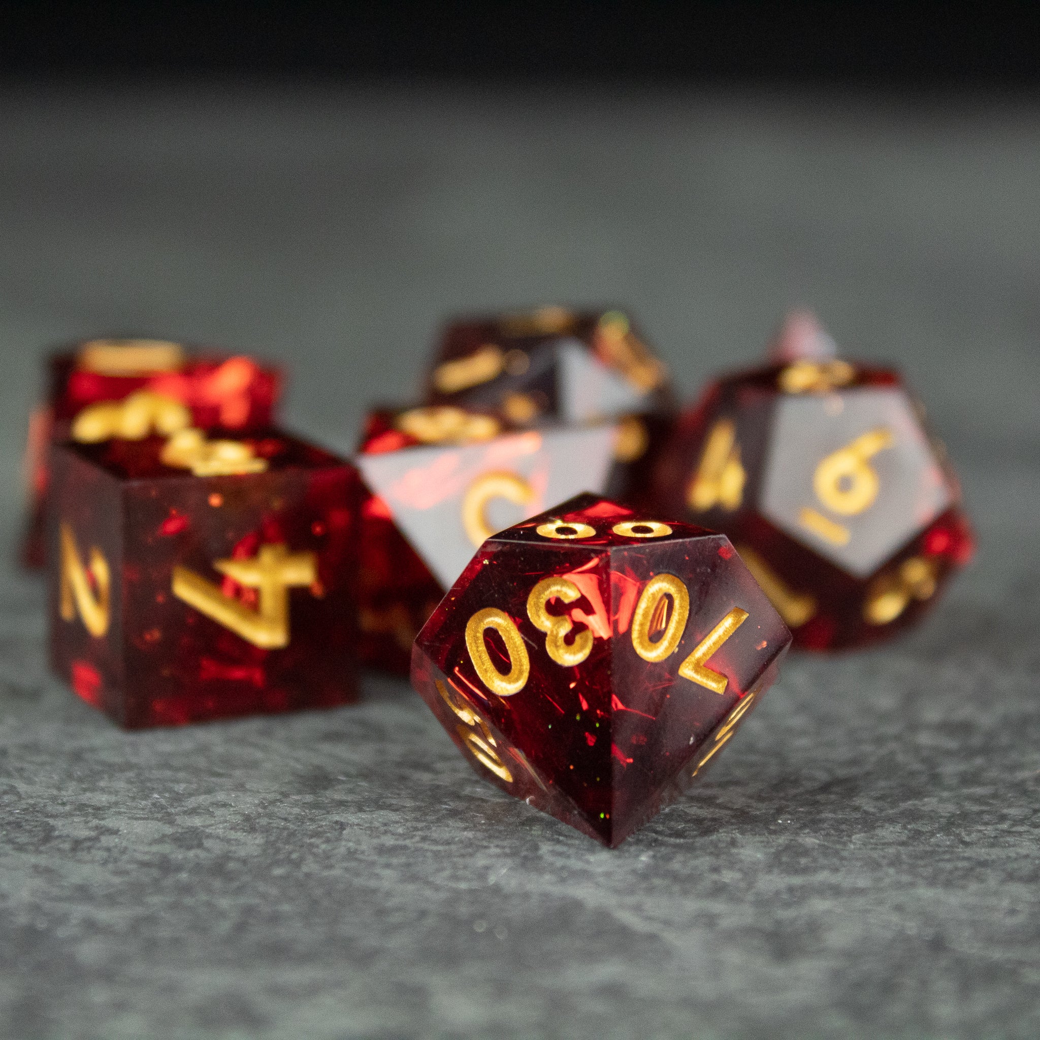 Ember Dice Set - Red translucent sharp-edged polyhedral dice with gold numbers, including a d20, d12, and d10.