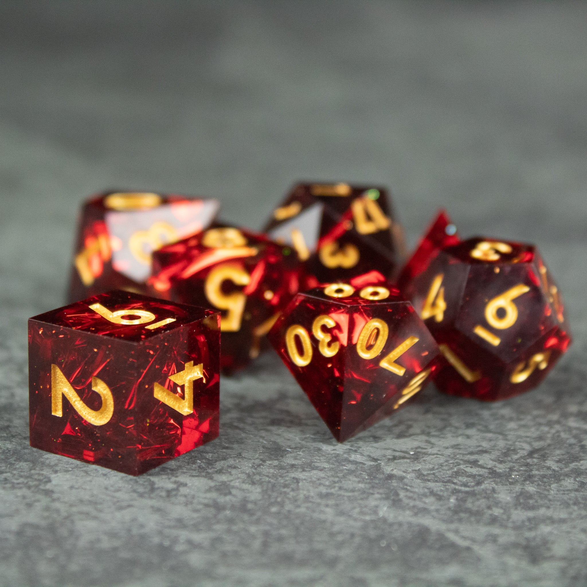 Ember Dice Set - Set of red, translucent polyhedral dice with sharp edges and gold numbers, glowing ember effect.