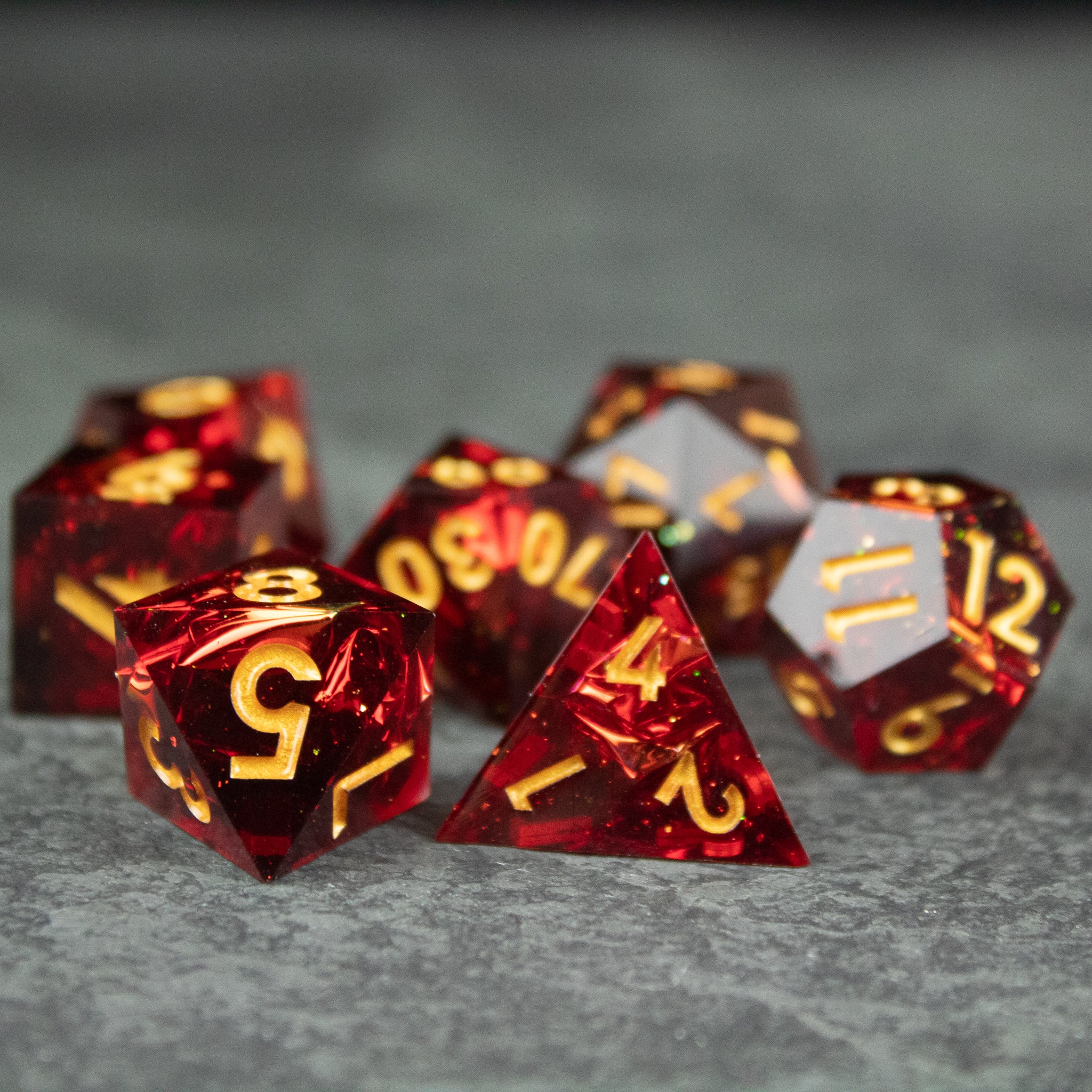 Ember Dice Set - Set of translucent red acrylic dice with sharp edges and gold numbers, including d20, d12, d10, d8, d6, and d4 shapes.