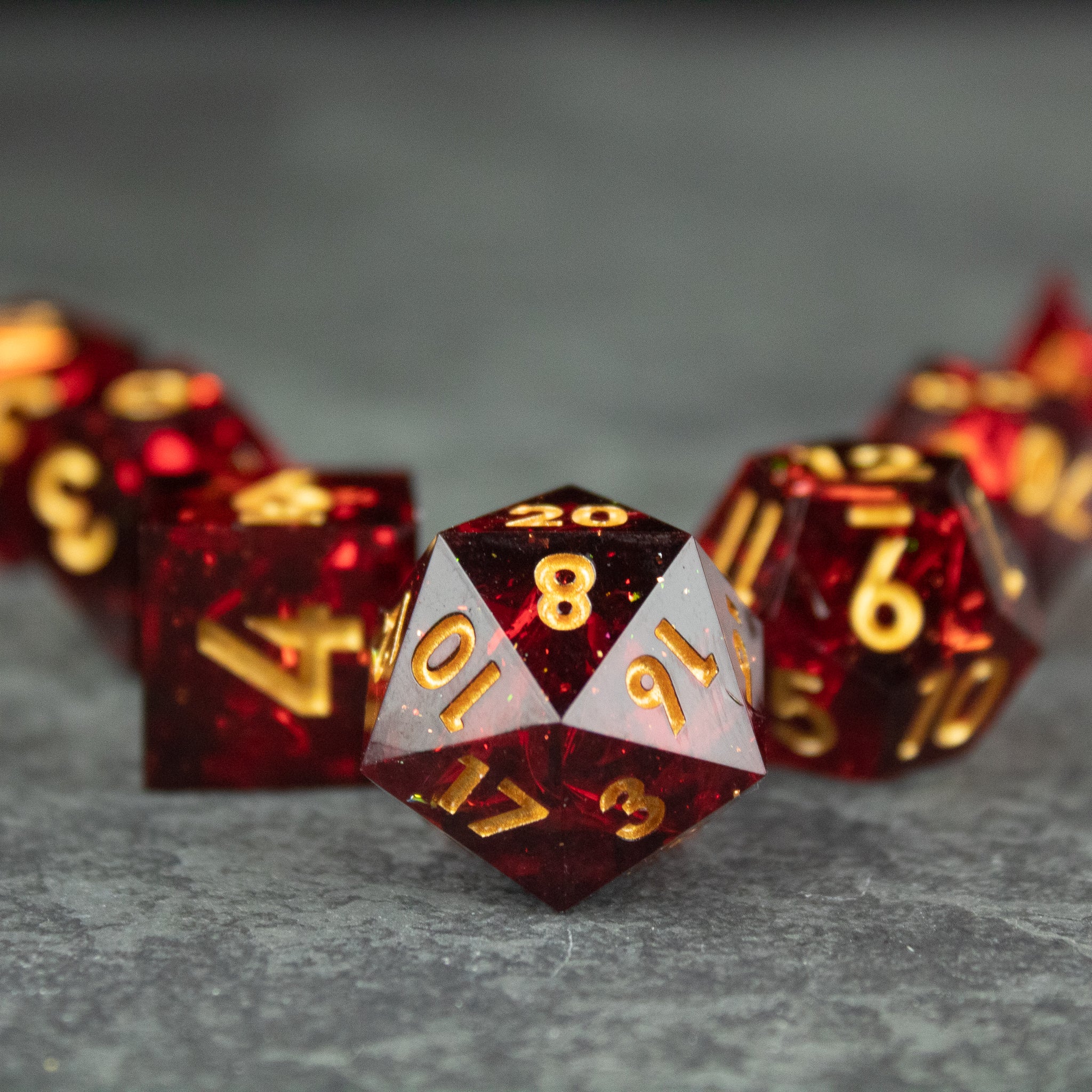 Ember Dice Set - Red sharp-edged polyhedral dice set with gold numbers on a gray surface.