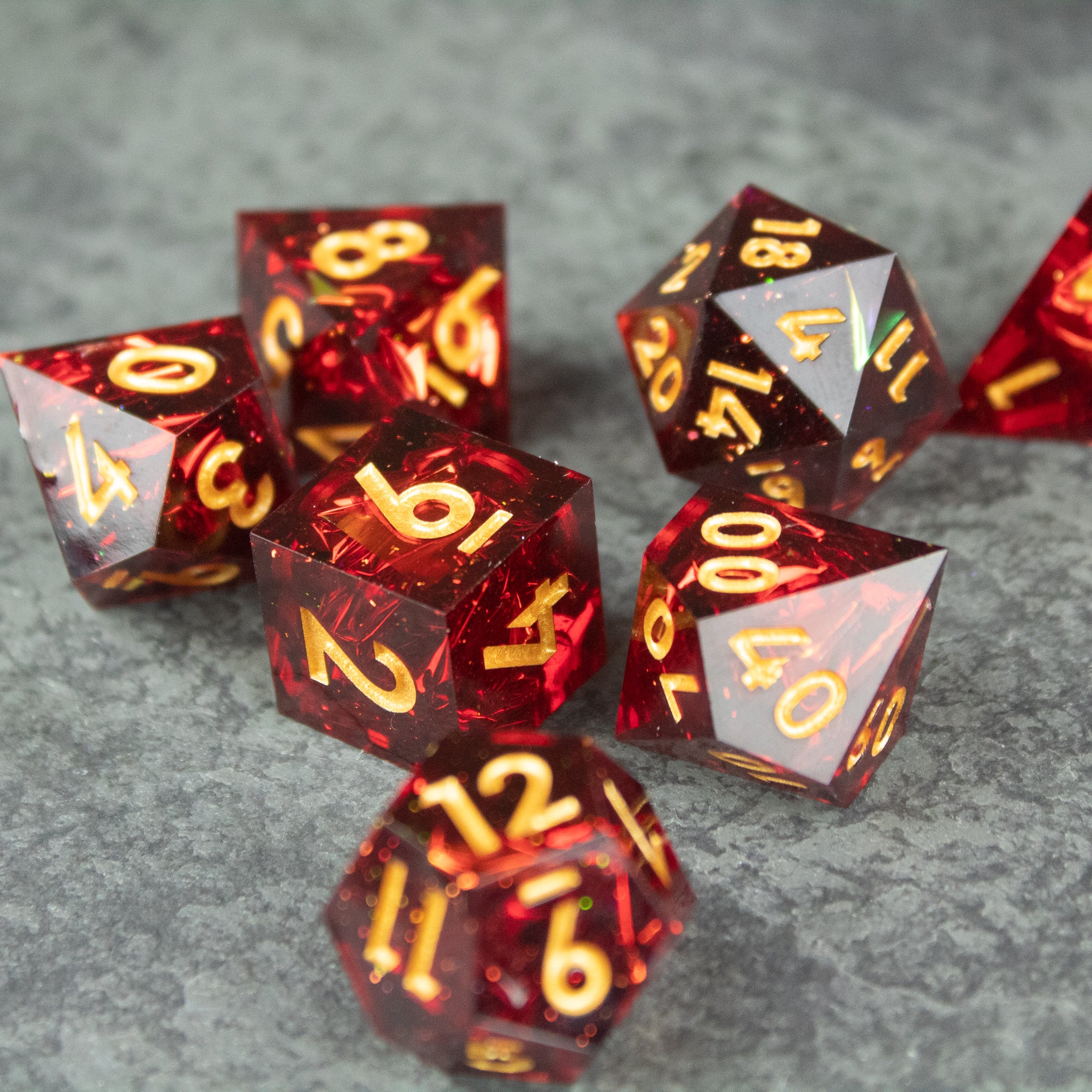 Ember Dice Set - Set of translucent red polyhedral dice with sharp edges and yellow-gold numbering on gray surface.