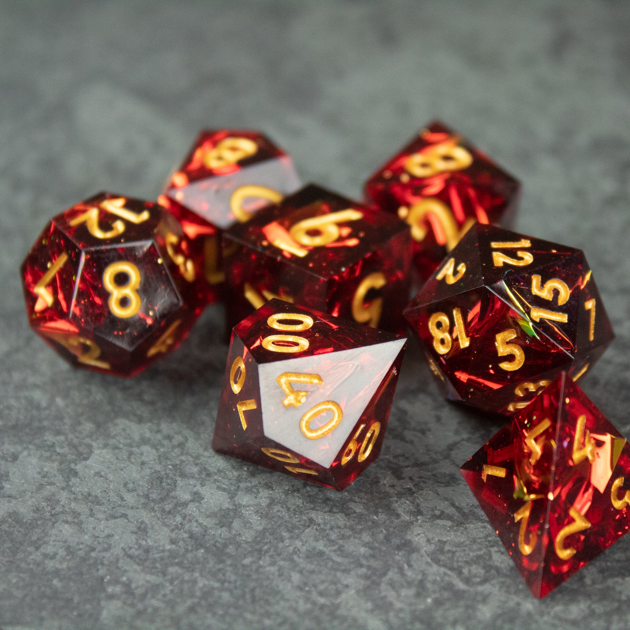 Ember Dice Set - Set of red translucent sharp-edged polyhedral dice with gold numbering, including a white d10 with gold numbers.