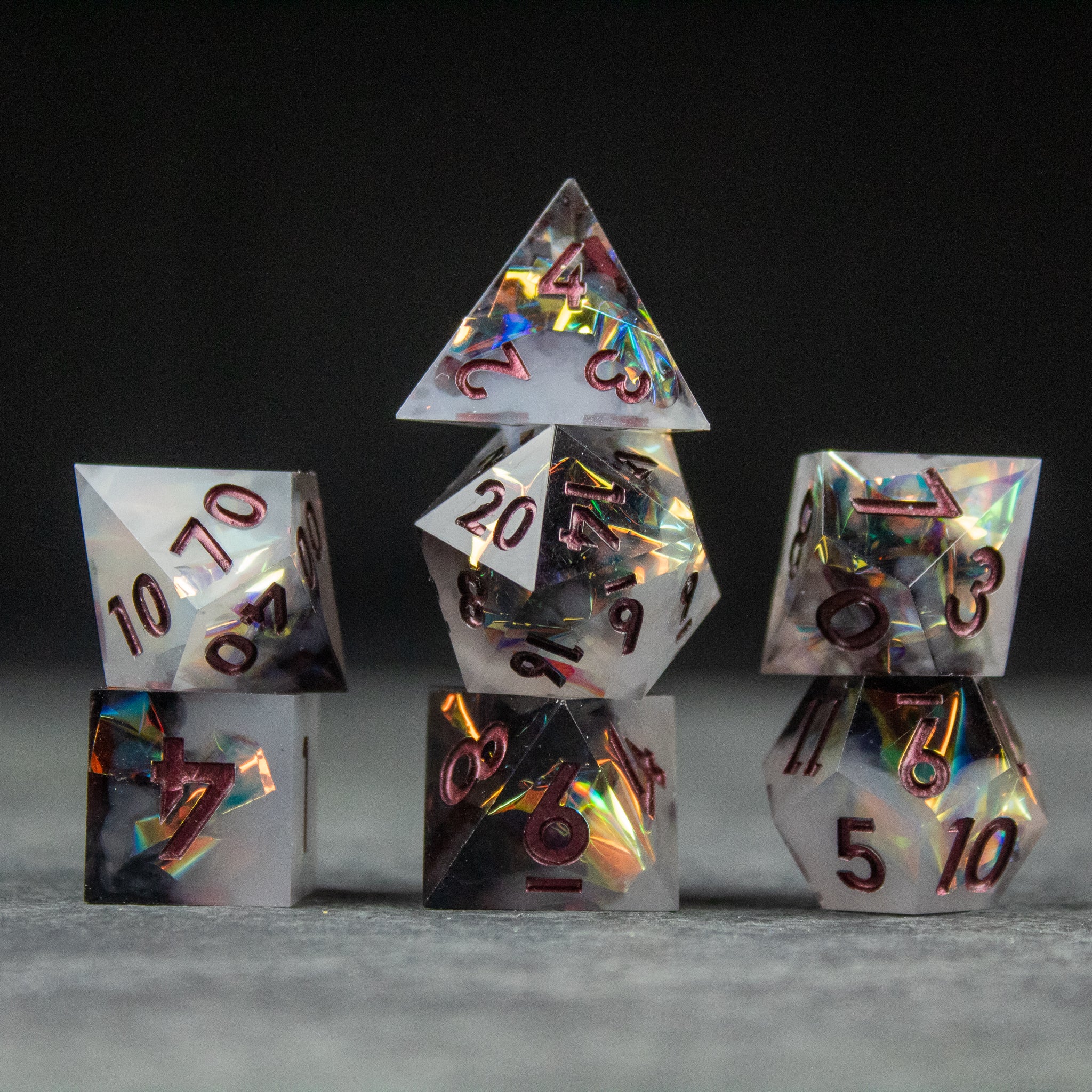 Oathbreaker Dice Set - Seven holographic sharp-edged dice with black numbers stacked on a gray surface against a black background.