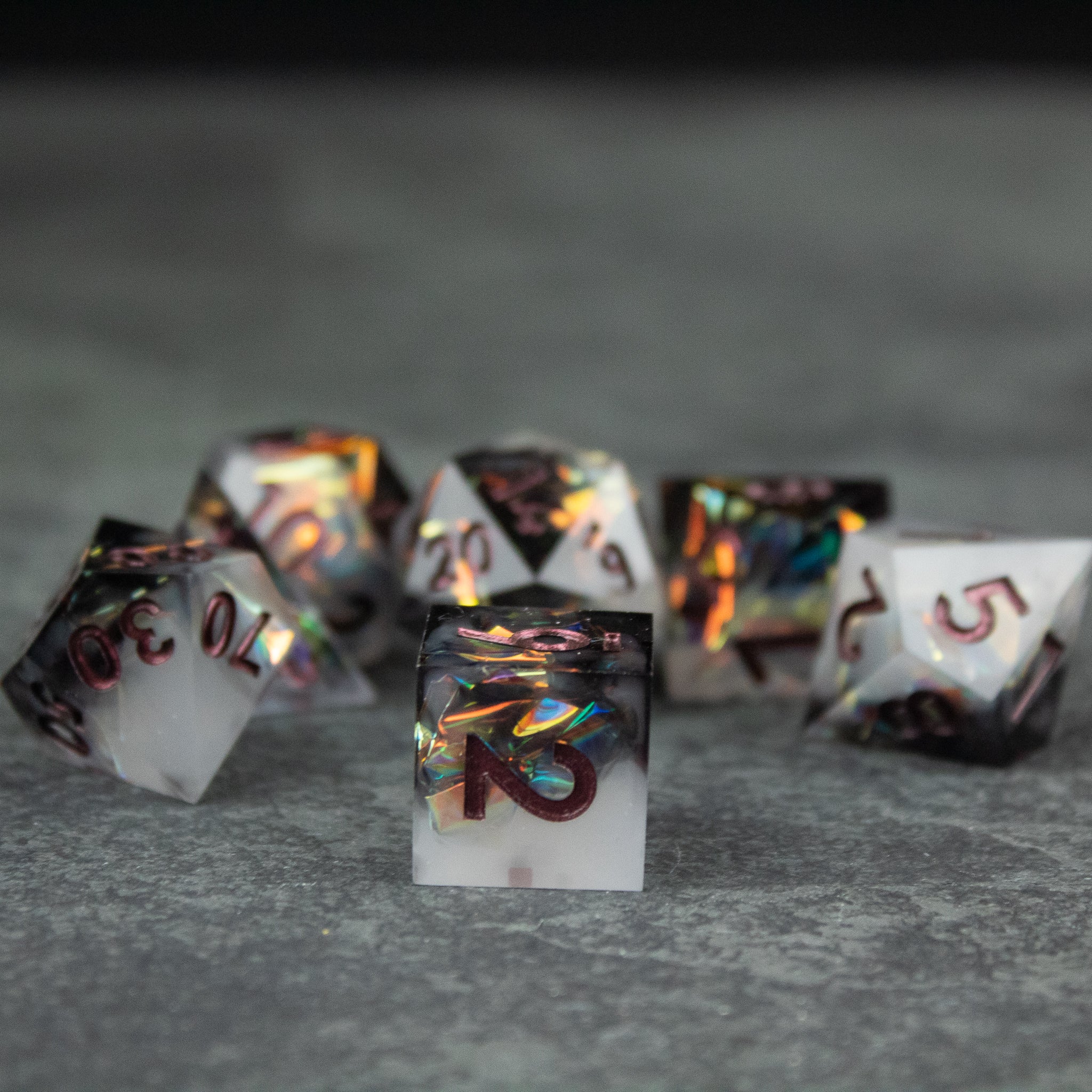 Oathbreaker Dice Set - Black and white sharp-edged polyhedral dice set with iridescent orange and blue numbers on a gray background.