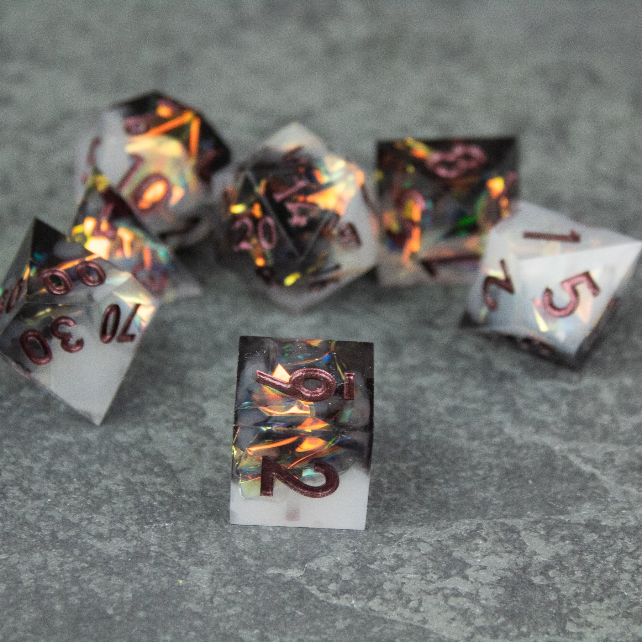 Oathbreaker Dice Set - Seven sharp-edged black and white dice with fiery, glowing orange-red numbers on a stone surface.