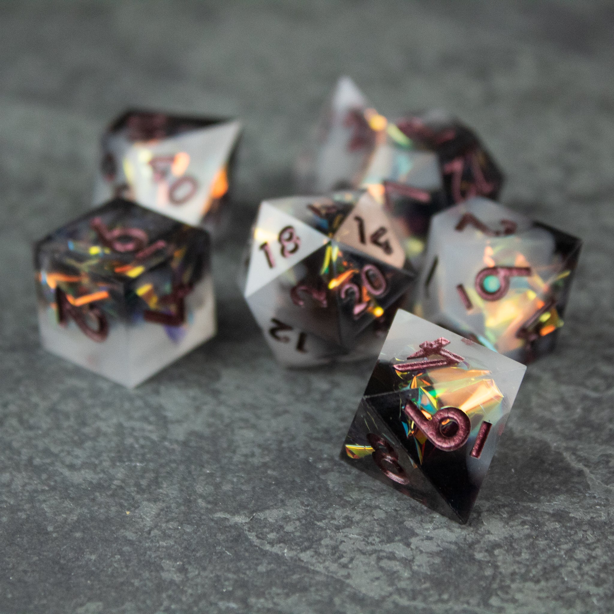 Oathbreaker Dice Set - Set of seven sharp-edged black and white polyhedral dice with iridescent, metallic numbering on a gray surface.