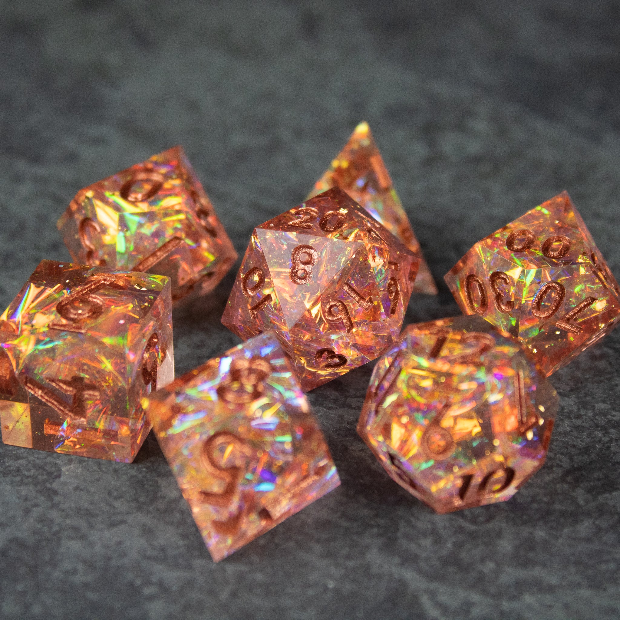 Sacred Flame Dice Set - Orange translucent sharp-edged polyhedral dice set with iridescent flakes on gray surface.