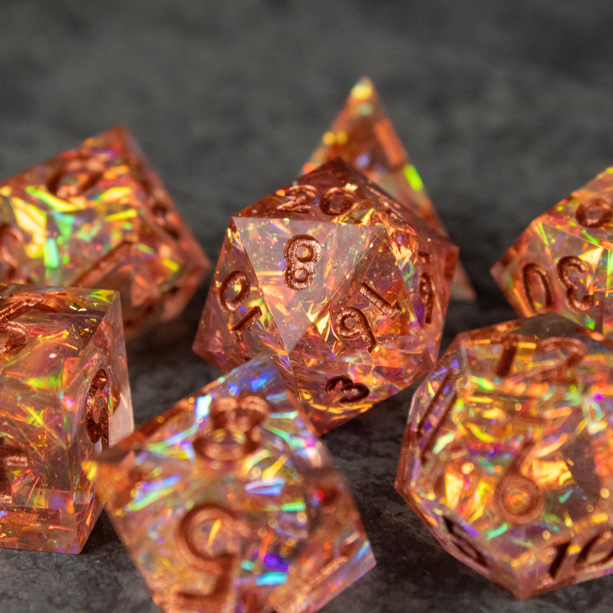 Sacred Flame Dice Set - Orange sharp-edged dice set with gold numbers and iridescent flakes inside, including a d20 and other polyhedral shapes.