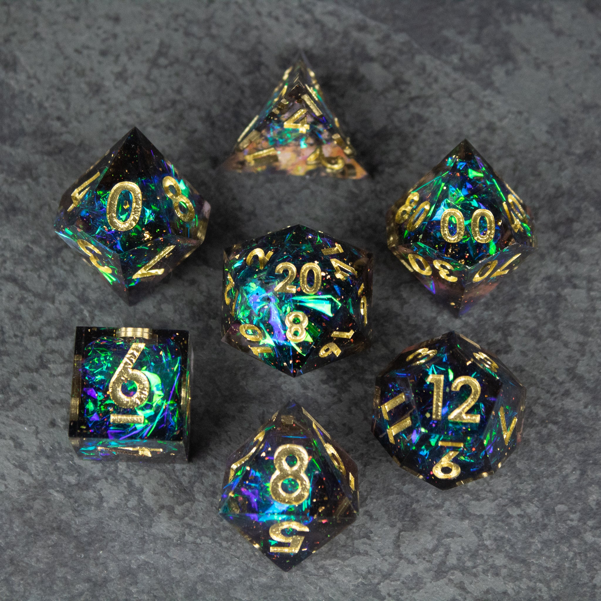 Galaxy Dice Set - Set of seven black sharp-edged dice with iridescent blue, green, and gold flecks and gold numbering.
