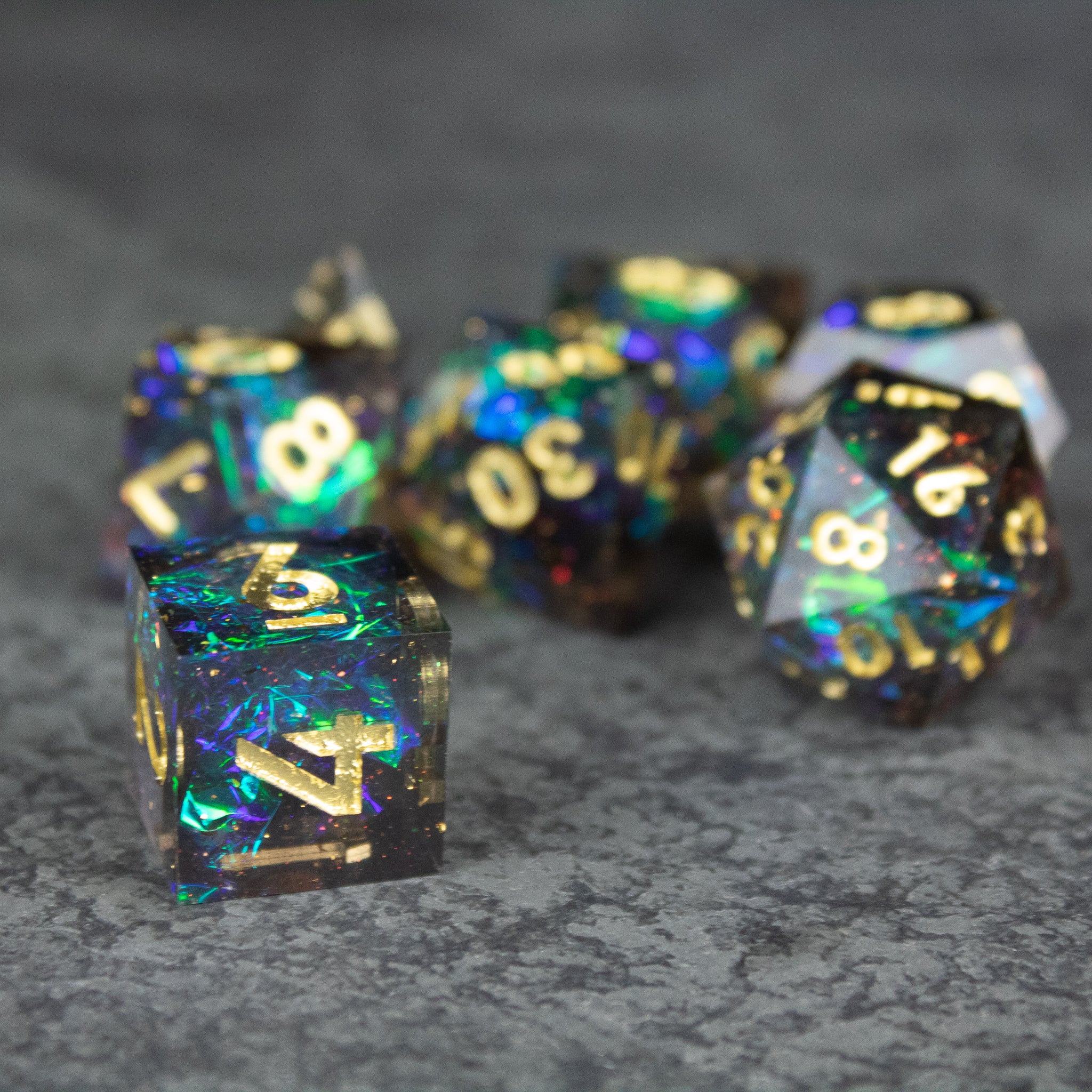 Galaxy Dice Set - Set of black transparent dice with sharp edges, filled with swirling blue and green galaxy-inspired colors and gold numbers.