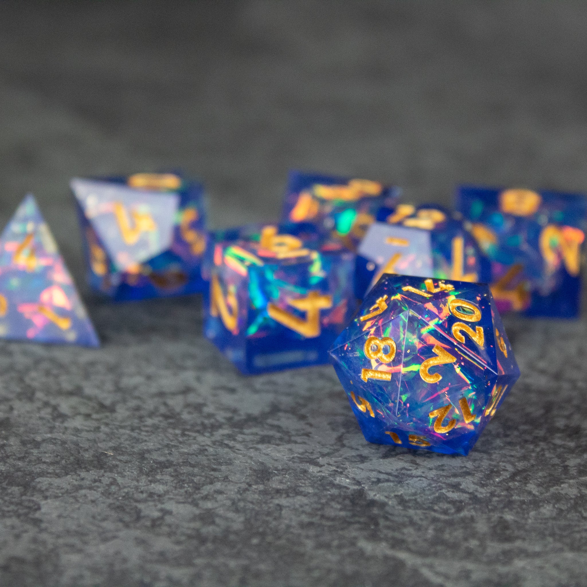 Arcana Dice Set - Set of blue sharp-edged polyhedral dice with gold numbers and colorful swirls.