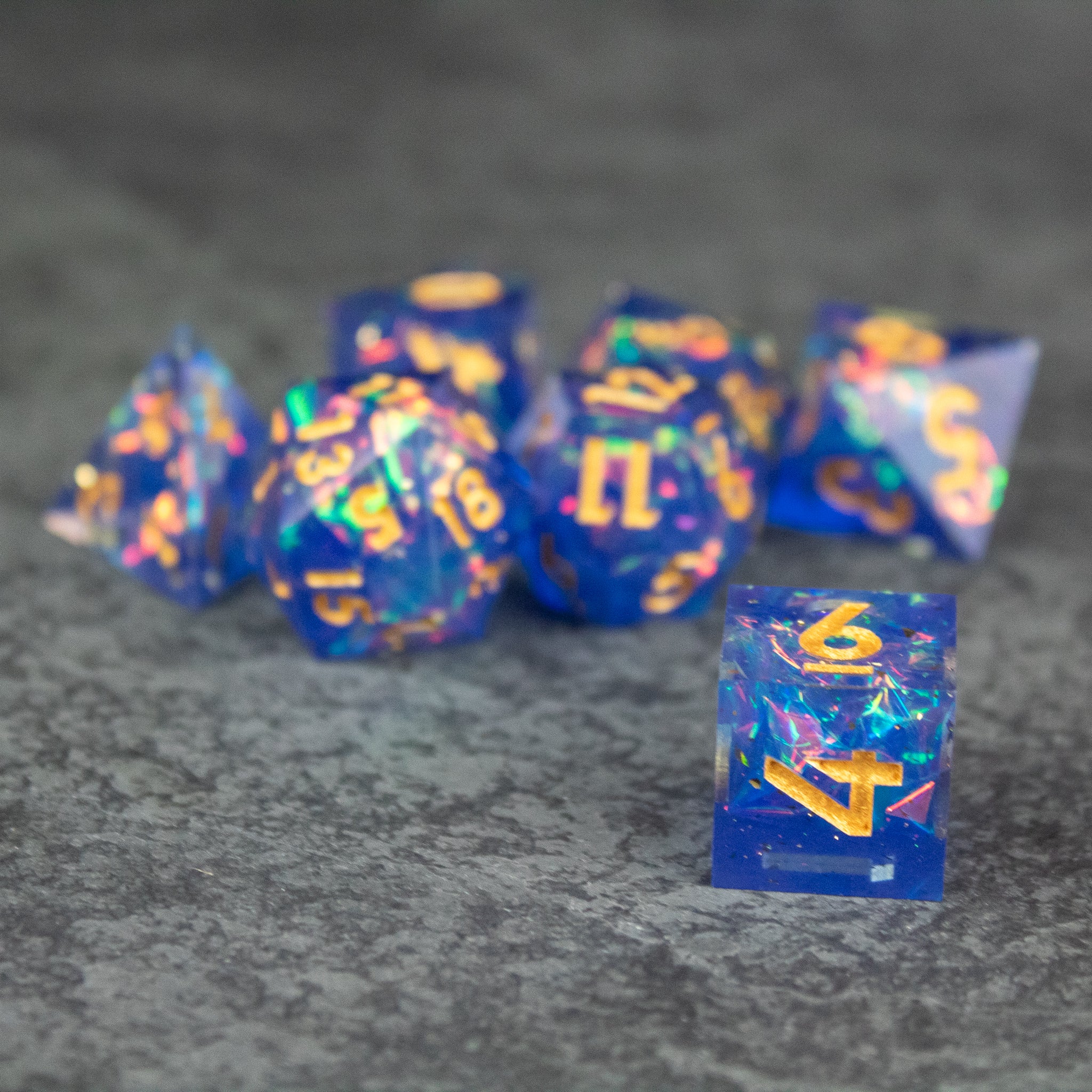 Arcana Dice Set - Blue sharp-edged polyhedral dice set with gold numbers on a dark textured background.
