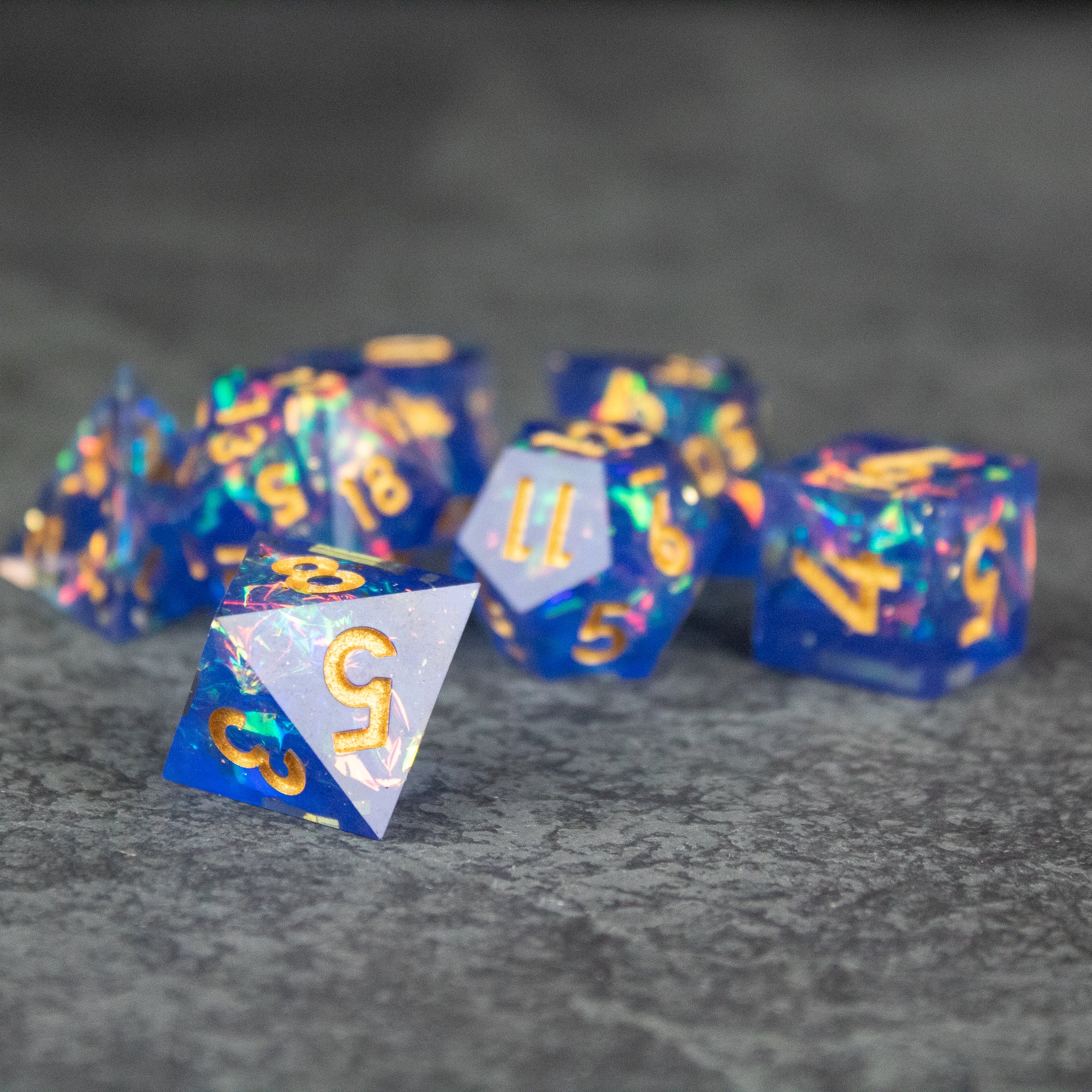 Arcana Dice Set - Blue sharp-edged polyhedral dice set with golden numbers and multicolor sparkles.