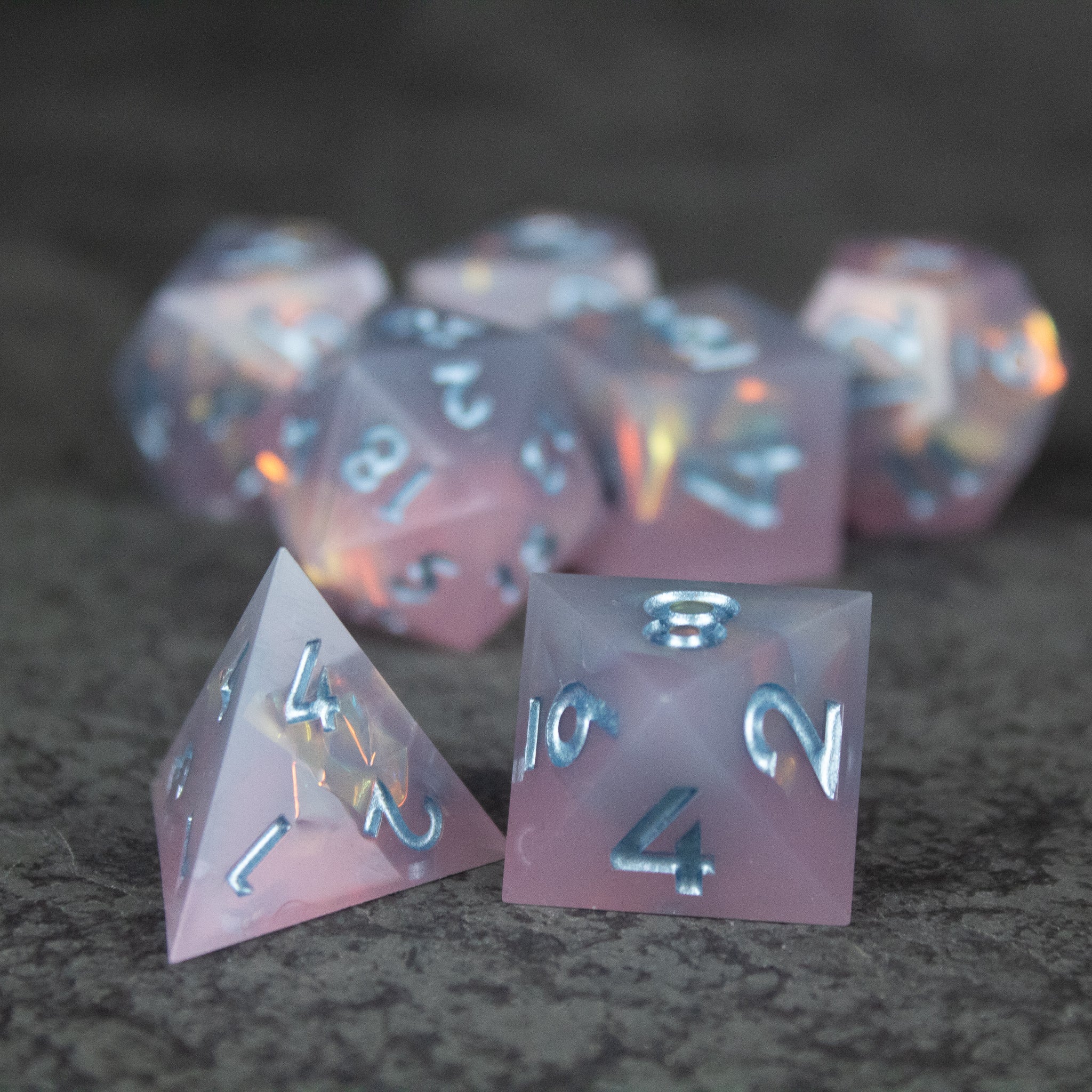 Moonshard Dice Set - Translucent pink sharp-edged polyhedral dice set with white numbering on a dark surface.
