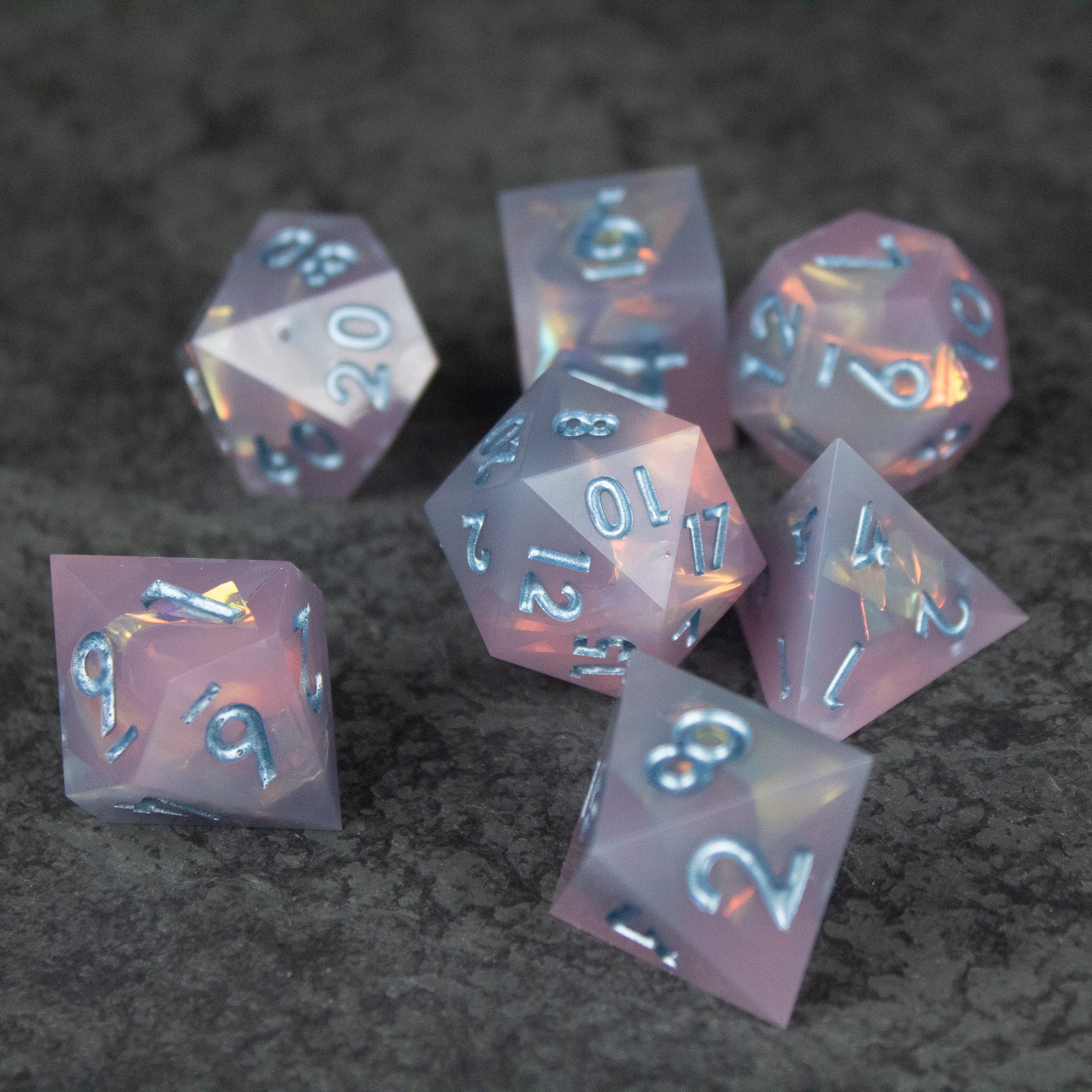 Moonshard Dice Set - Translucent pink sharp-edged polyhedral dice set with white numbering on dark gray surface.