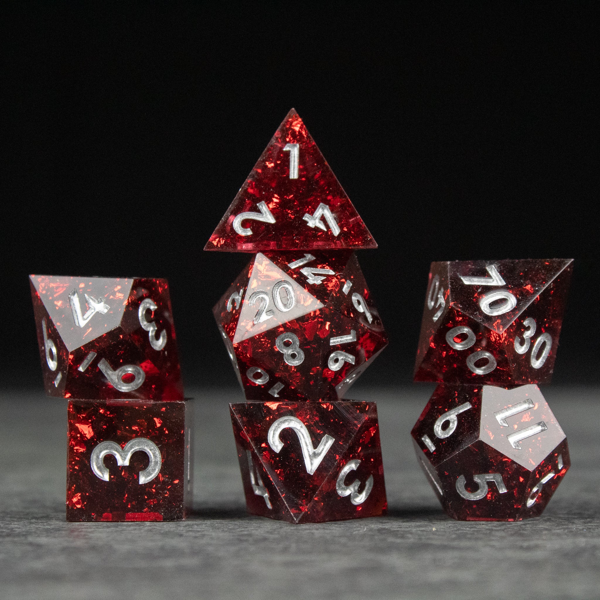Inferno Dice Set - Set of seven sharp-edged red translucent dice with white numbers on a dark surface.