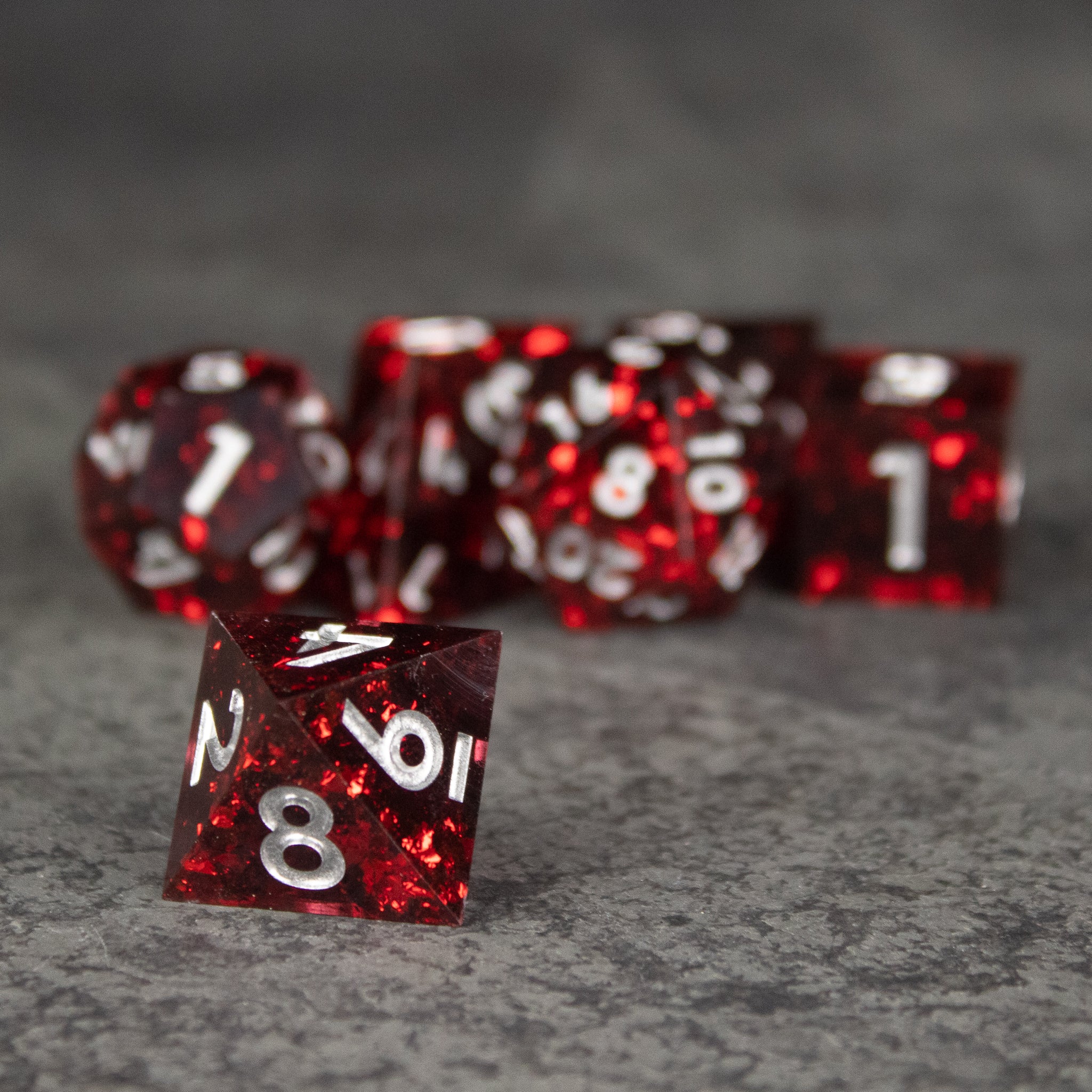 Inferno Dice Set - Set of glossy red sharp-edged polyhedral dice with white numbers on a gray surface.