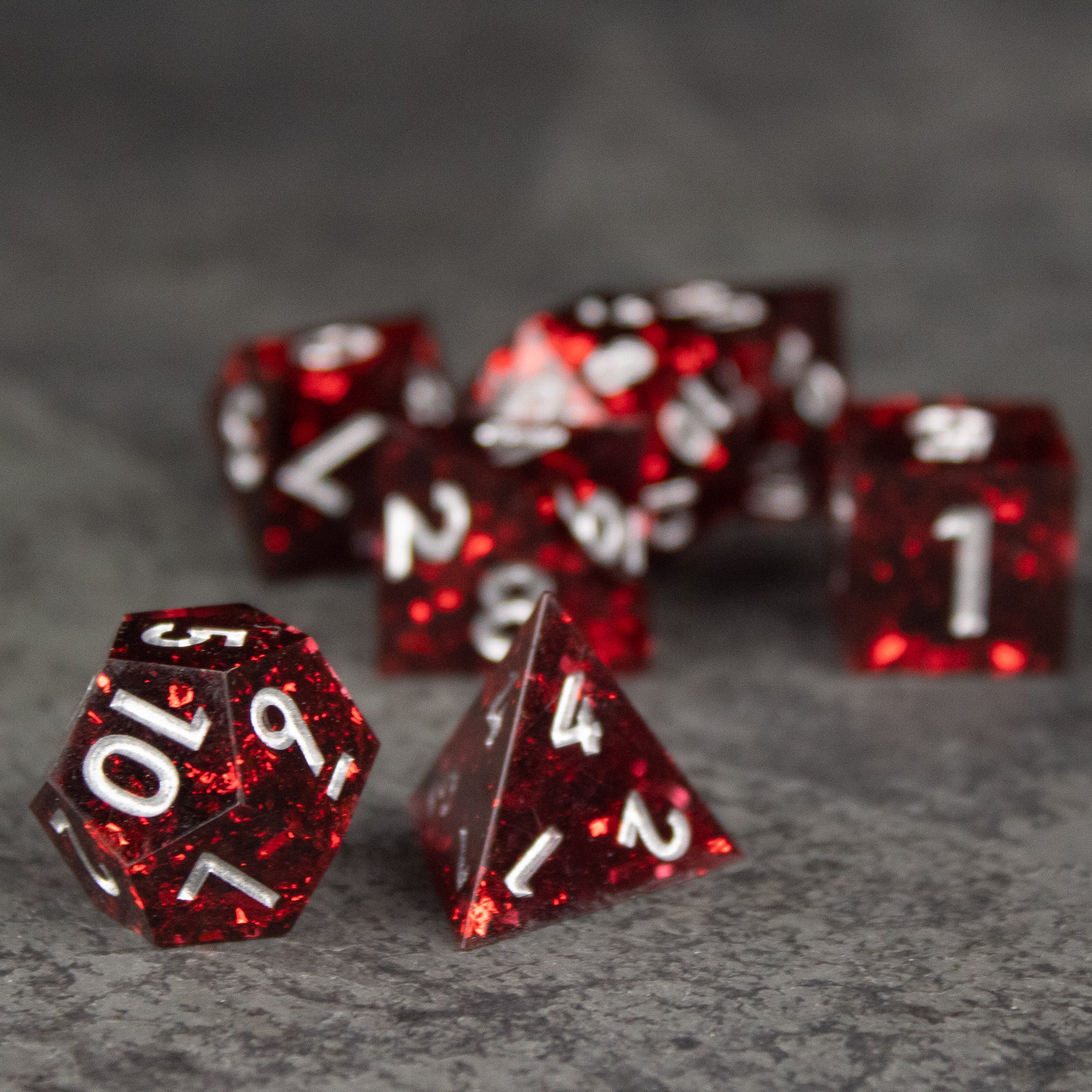 Inferno Dice Set - Red translucent sharp-edged polyhedral dice set with white numbering on gray surface.