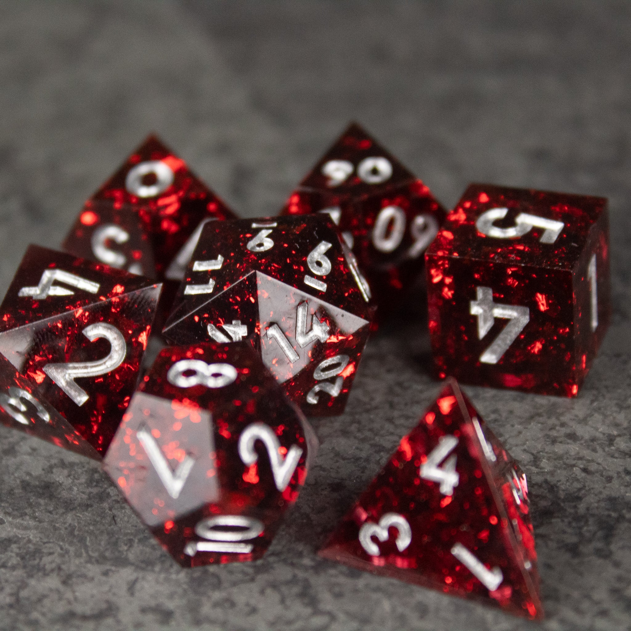 Inferno Dice Set - Seven red translucent sharp-edged polyhedral dice with white numbers on a gray surface.