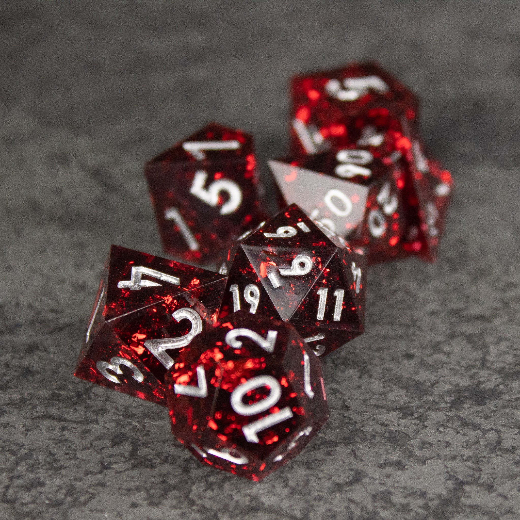 Inferno Dice Set - Glossy translucent red polyhedral dice set with sharp edges and white numbering on gray surface.