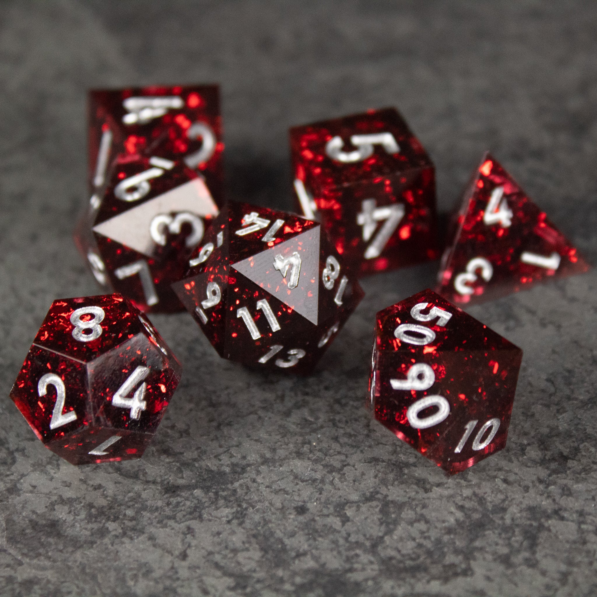 Inferno Dice Set - Set of seven translucent red polyhedral dice with sharp edges and white numbers on a gray textured surface.