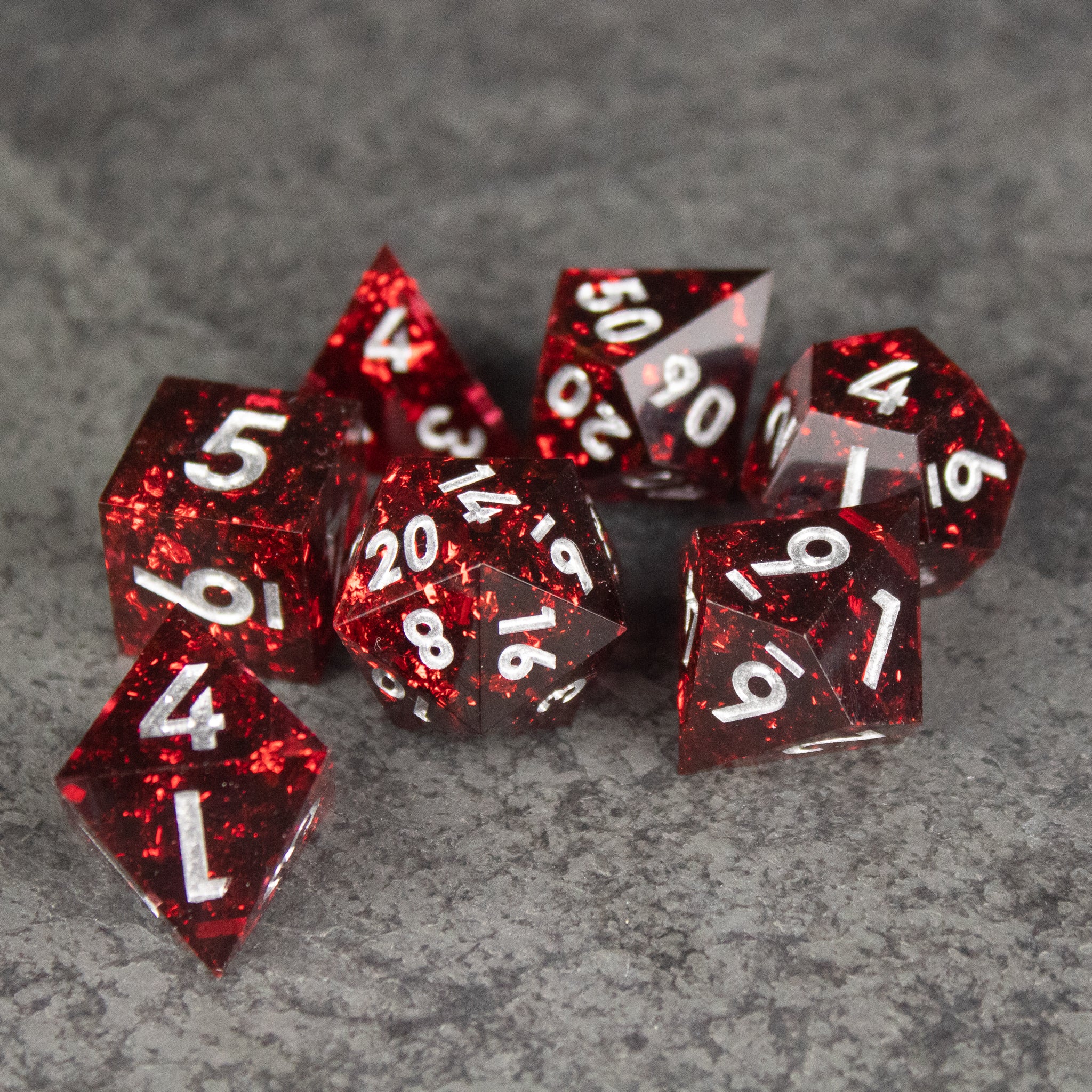 Inferno Dice Set - Set of translucent red sharp-edged polyhedral dice with white numbers on gray stone surface.