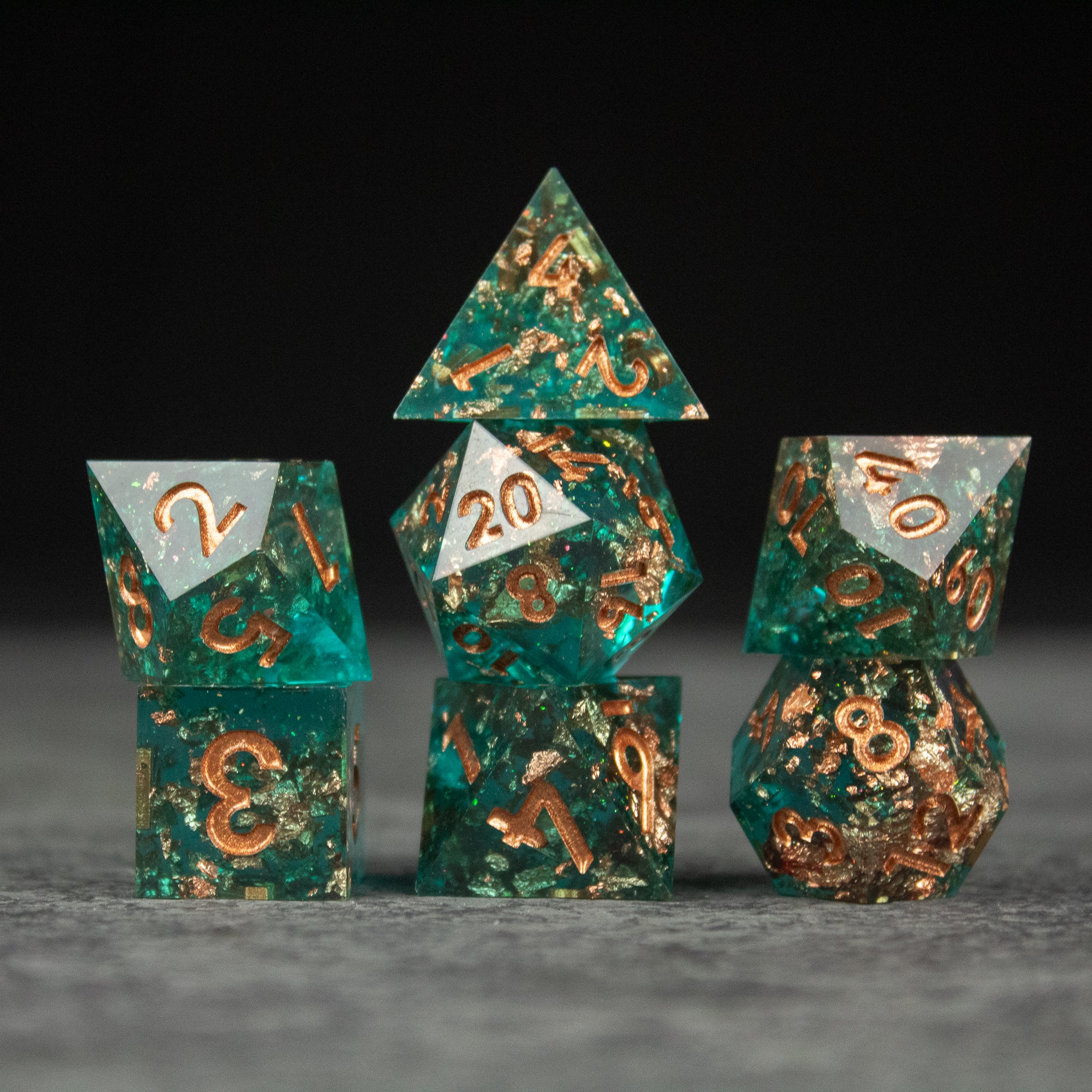 Oasis Dice Set - Green sharp-edged polyhedral dice set with gold flecks and white numbering on gray surface.