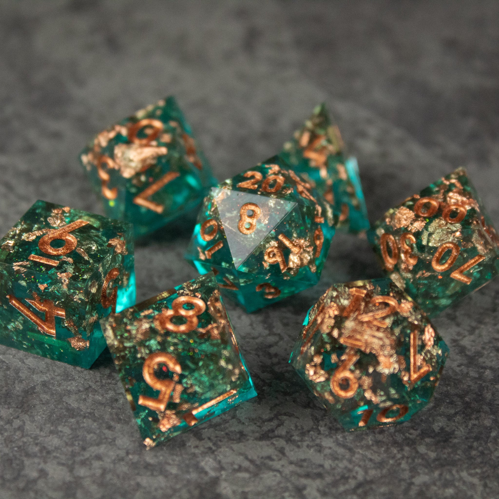 Oasis Dice Set - Seven translucent green polyhedral dice with sharp edges and gold metallic numbers on a gray textured surface.