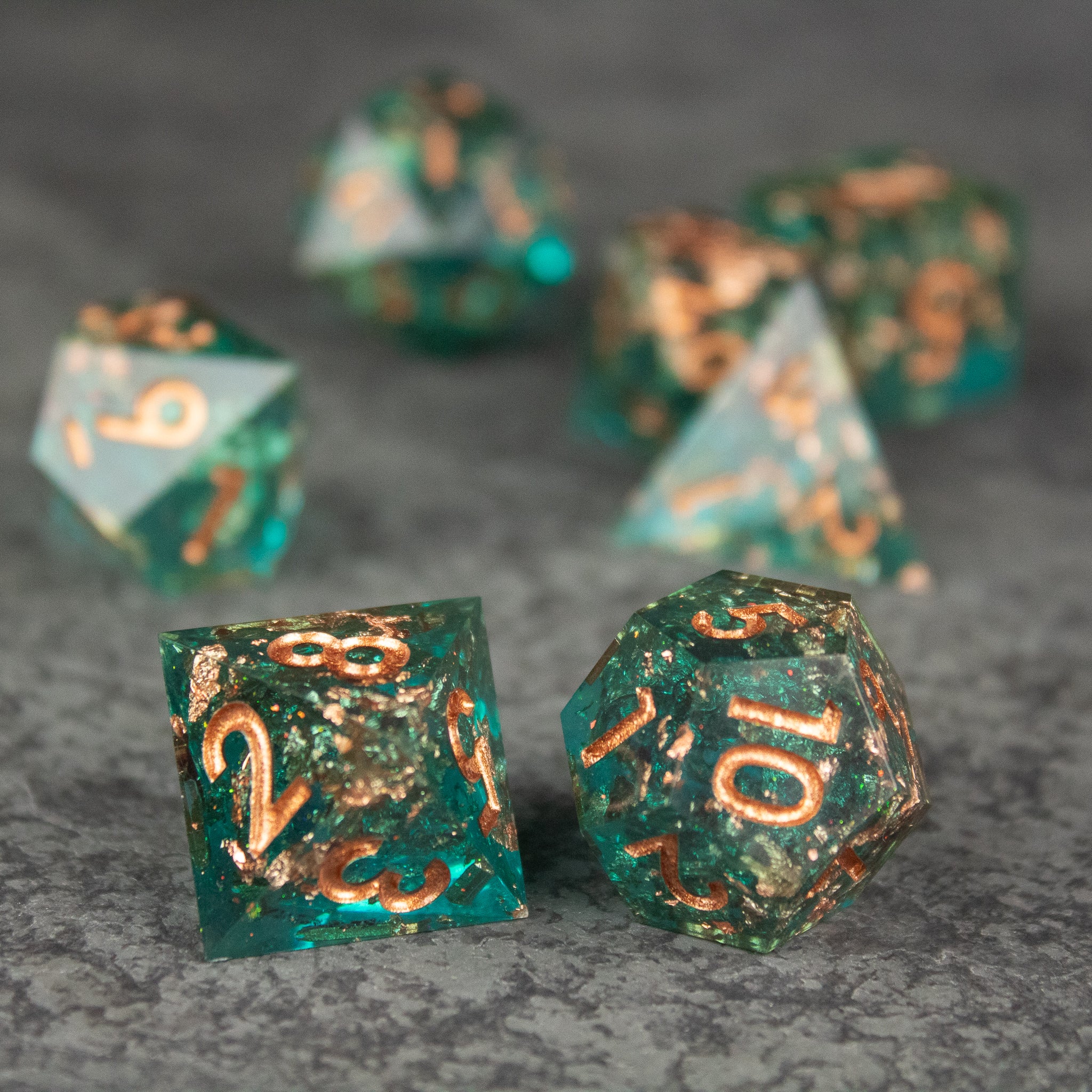 Oasis Dice Set - Translucent green polyhedral dice set with sharp edges and gold numbering on a gray surface.
