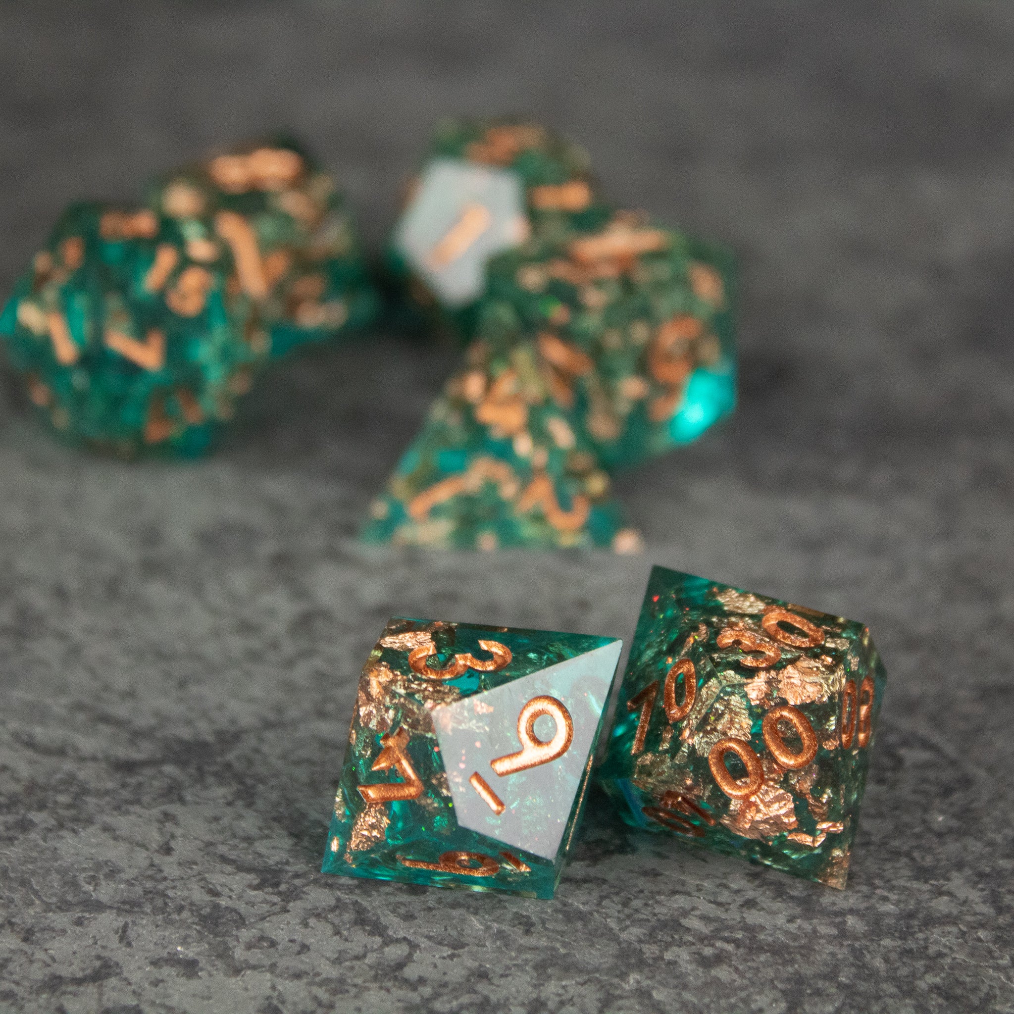 Oasis Dice Set - Green sharp-edged dice with copper flakes, featuring white numbers, set on gray surface.