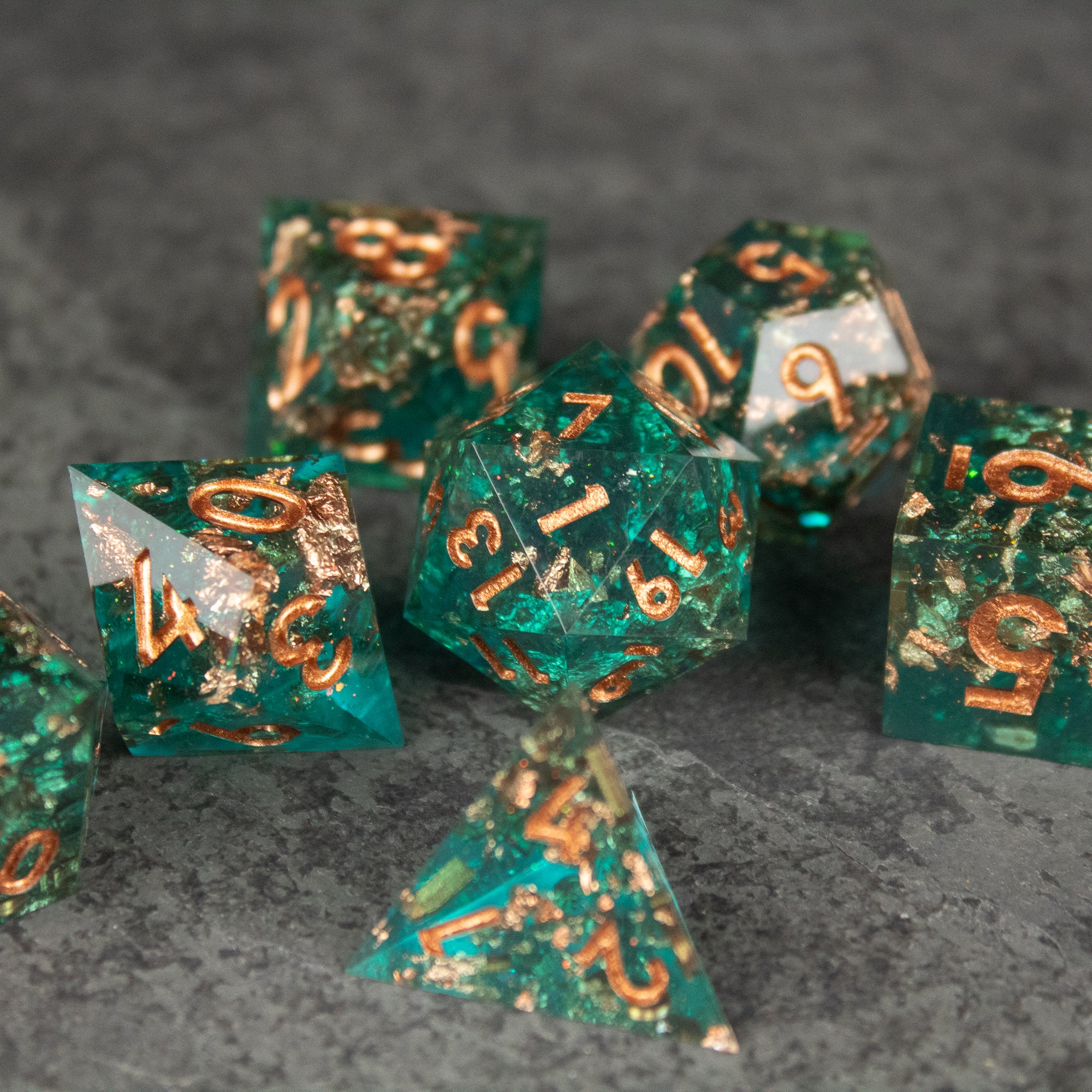 Oasis Dice Set - Green transparent sharp-edged polyhedral dice set with gold numbering on a gray surface.