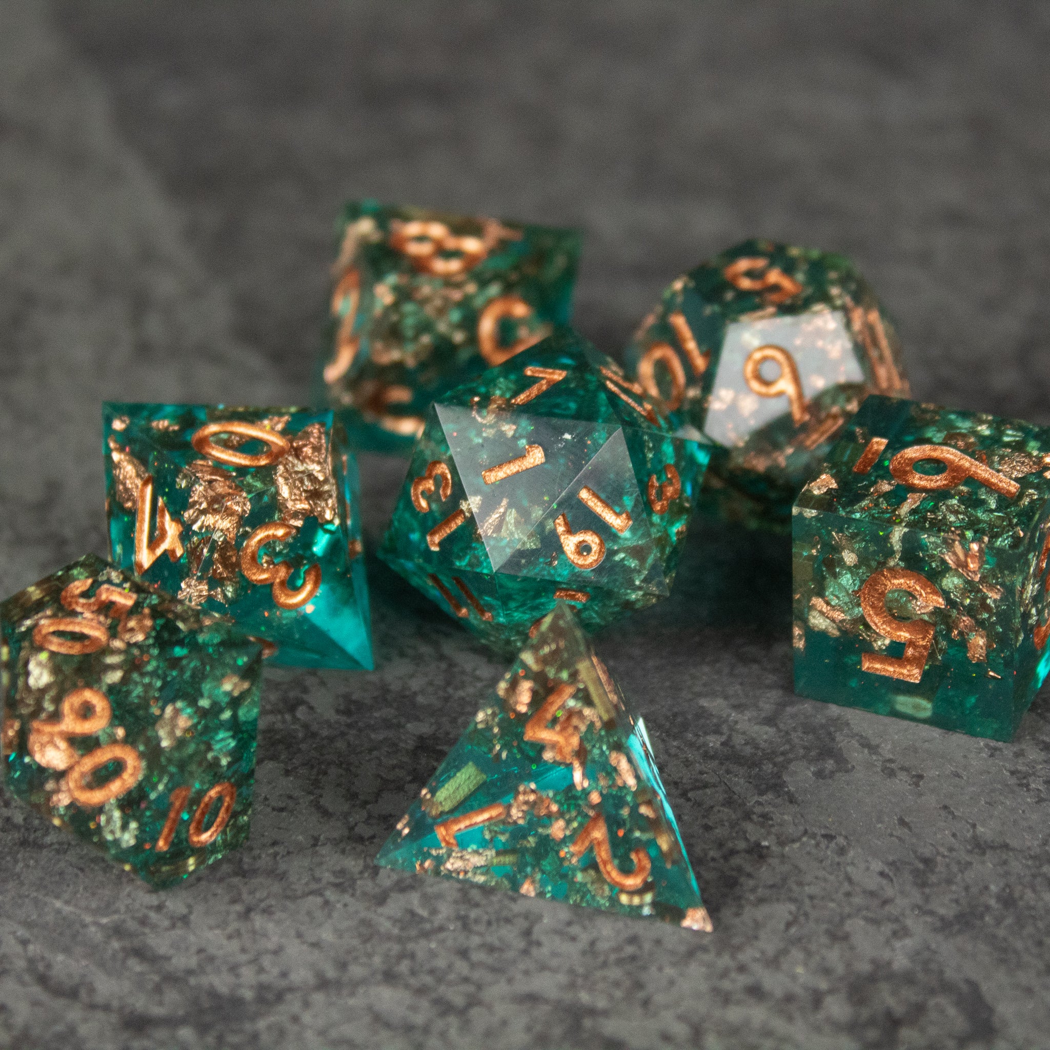 Oasis Dice Set - Set of seven translucent green polyhedral dice with gold numbers and sharp edges on a dark textured surface.