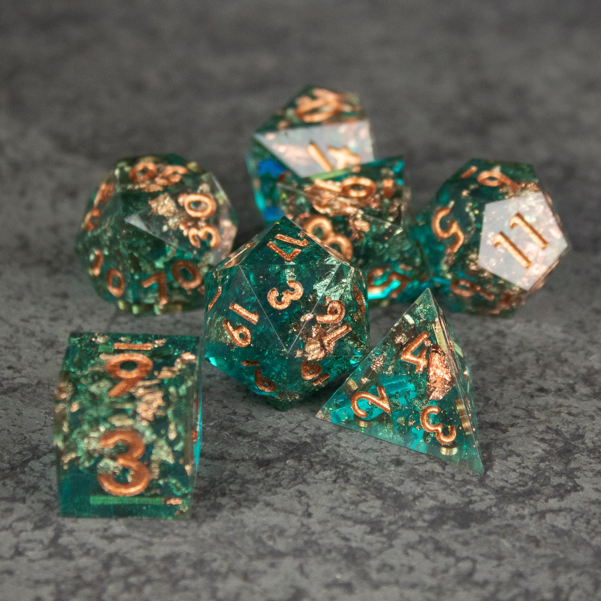 Oasis Dice Set - Translucent green polyhedral dice set with sharp edges and gold numbering on a gray textured surface.