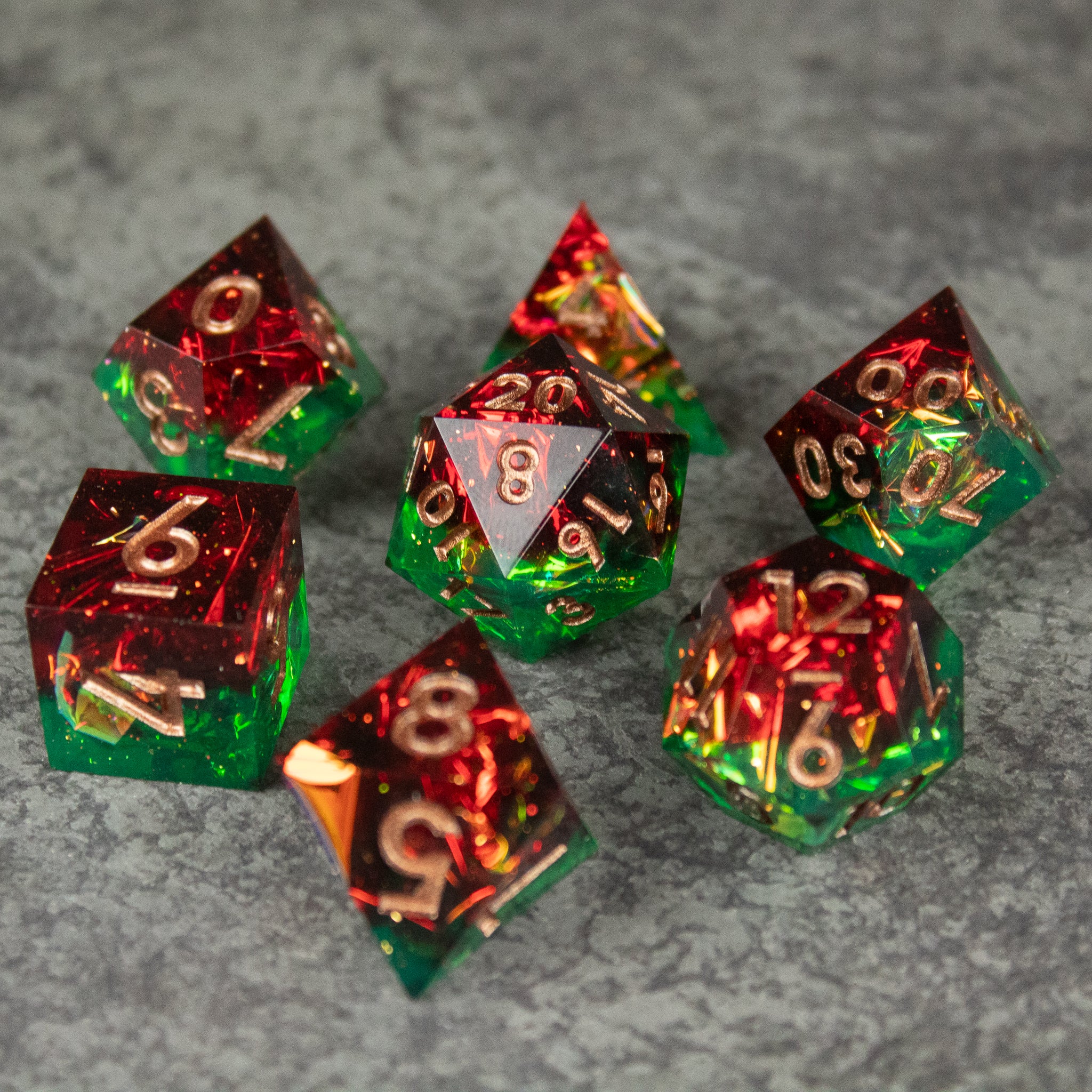 Jungle Fire Dice Set - Seven sharp-edged polyhedral dice in translucent red and green with gold numbers, designed for tabletop games.