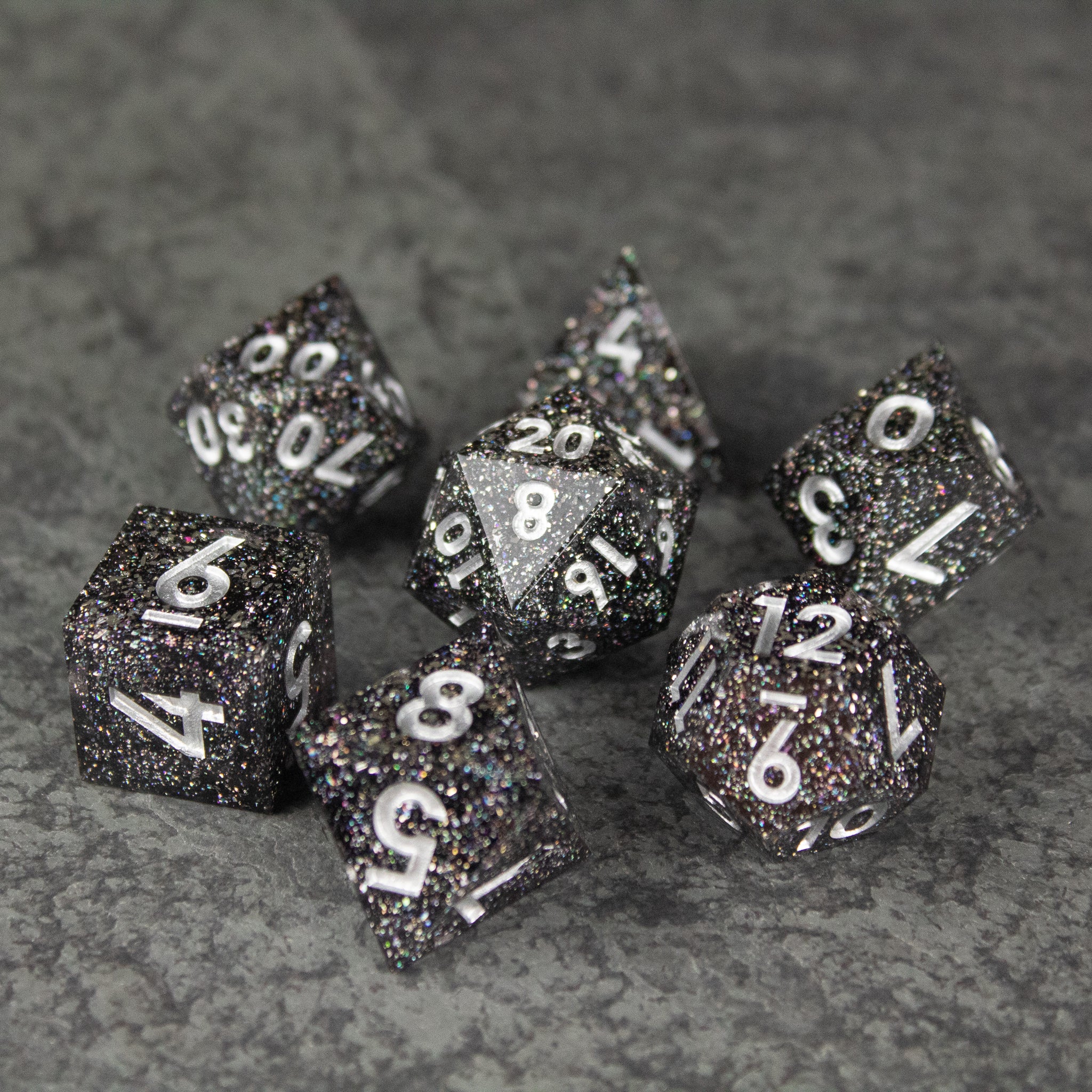 Starfield Dice Set - Black speckled seven-piece dice set with white numbering and sharp edges on gray surface.