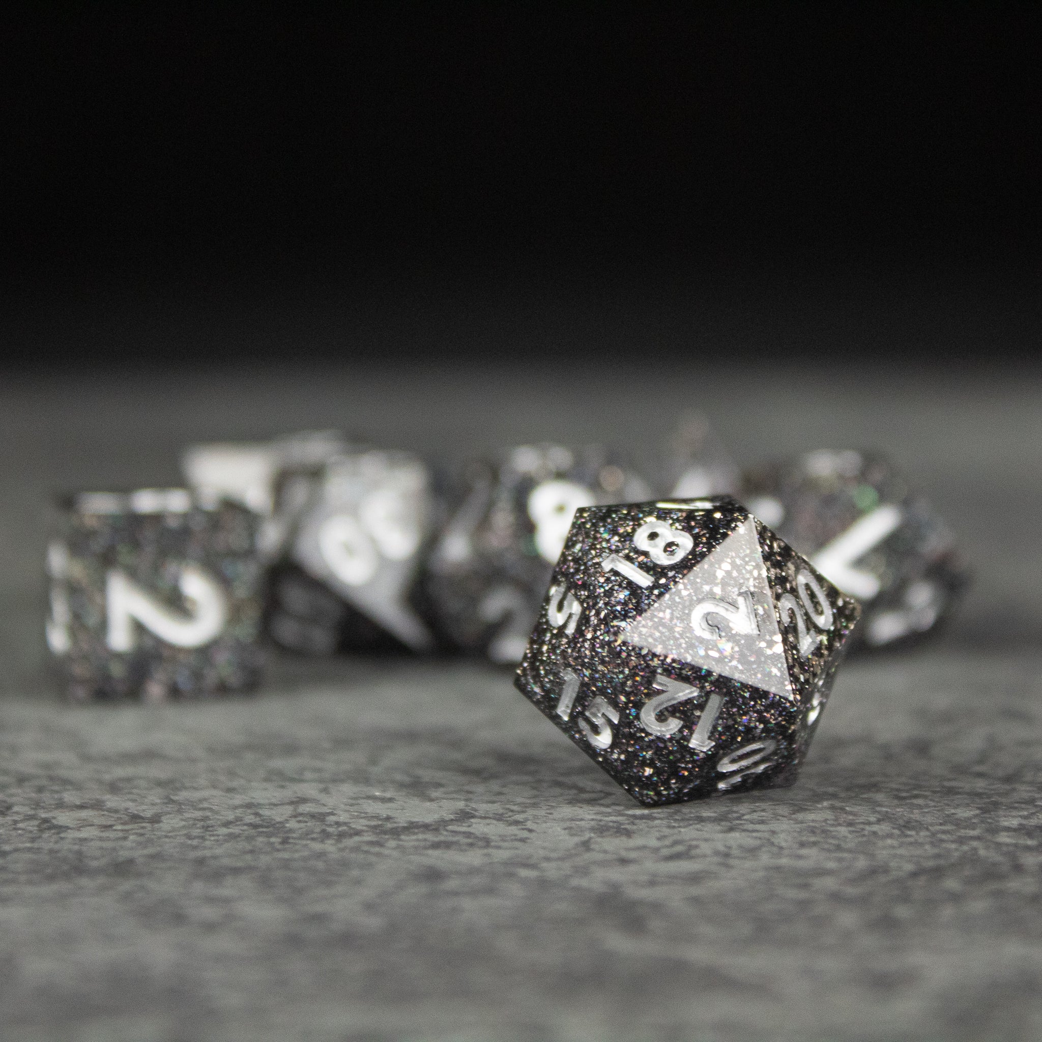 Starfield Dice Set - Black and white speckled 20-sided dice set with sharp edges and white numbering on a gray surface.