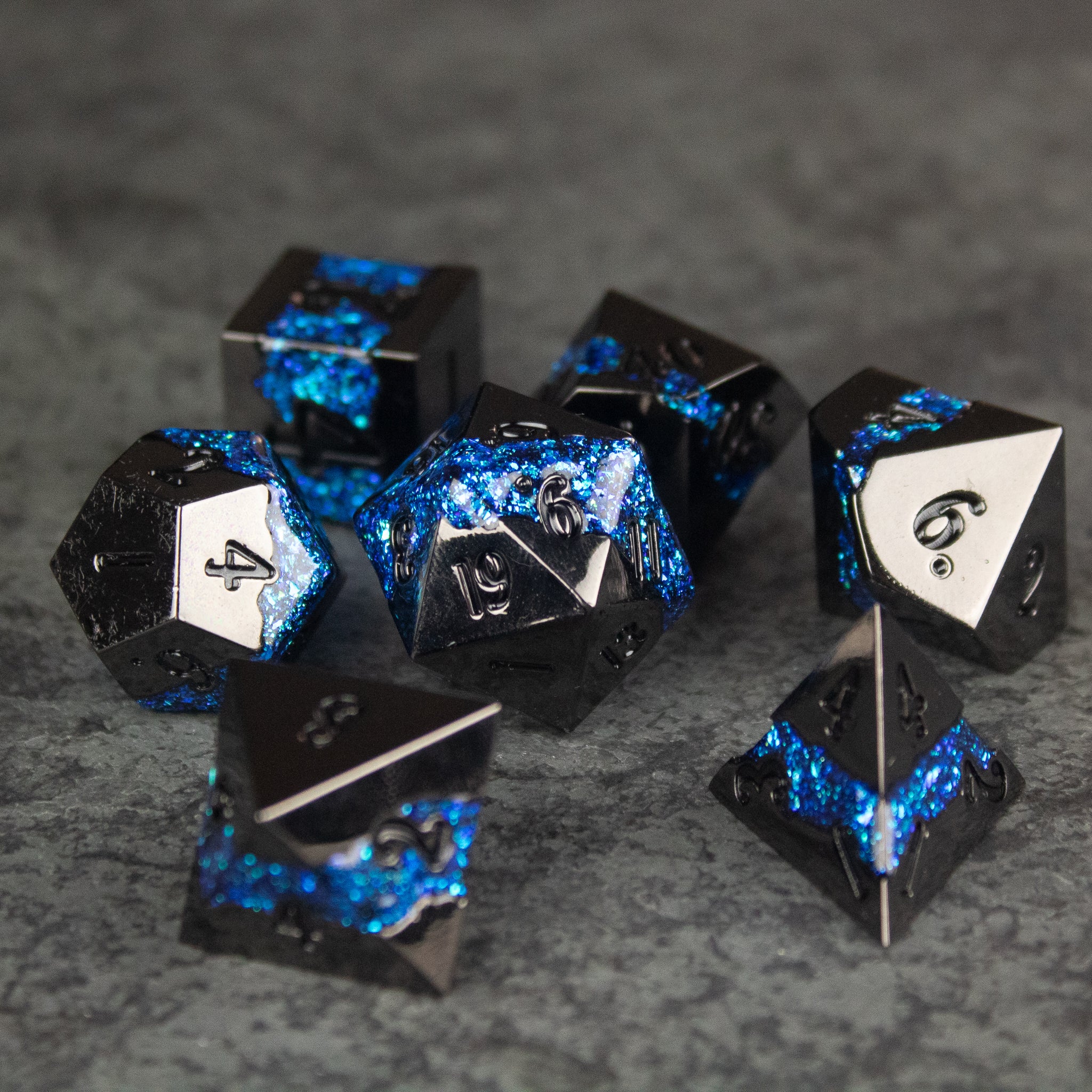 Blue Rift Dice Set - Set of seven black metal dice with vibrant blue glitter-filled rift patterns and white numbering.