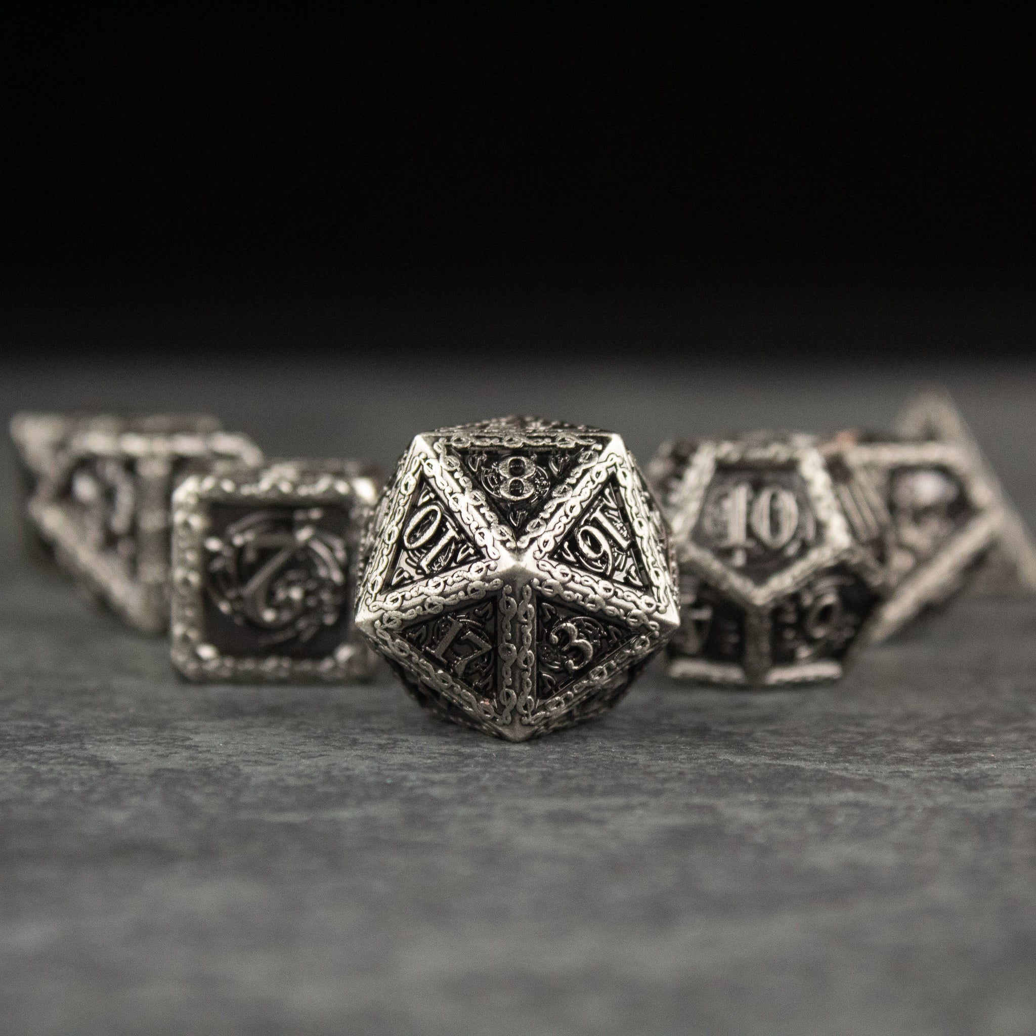 Bardic Inspiration Metal Dice Set - Silver metal polyhedral dice set with ornate, intricate designs and black engraved numbers.