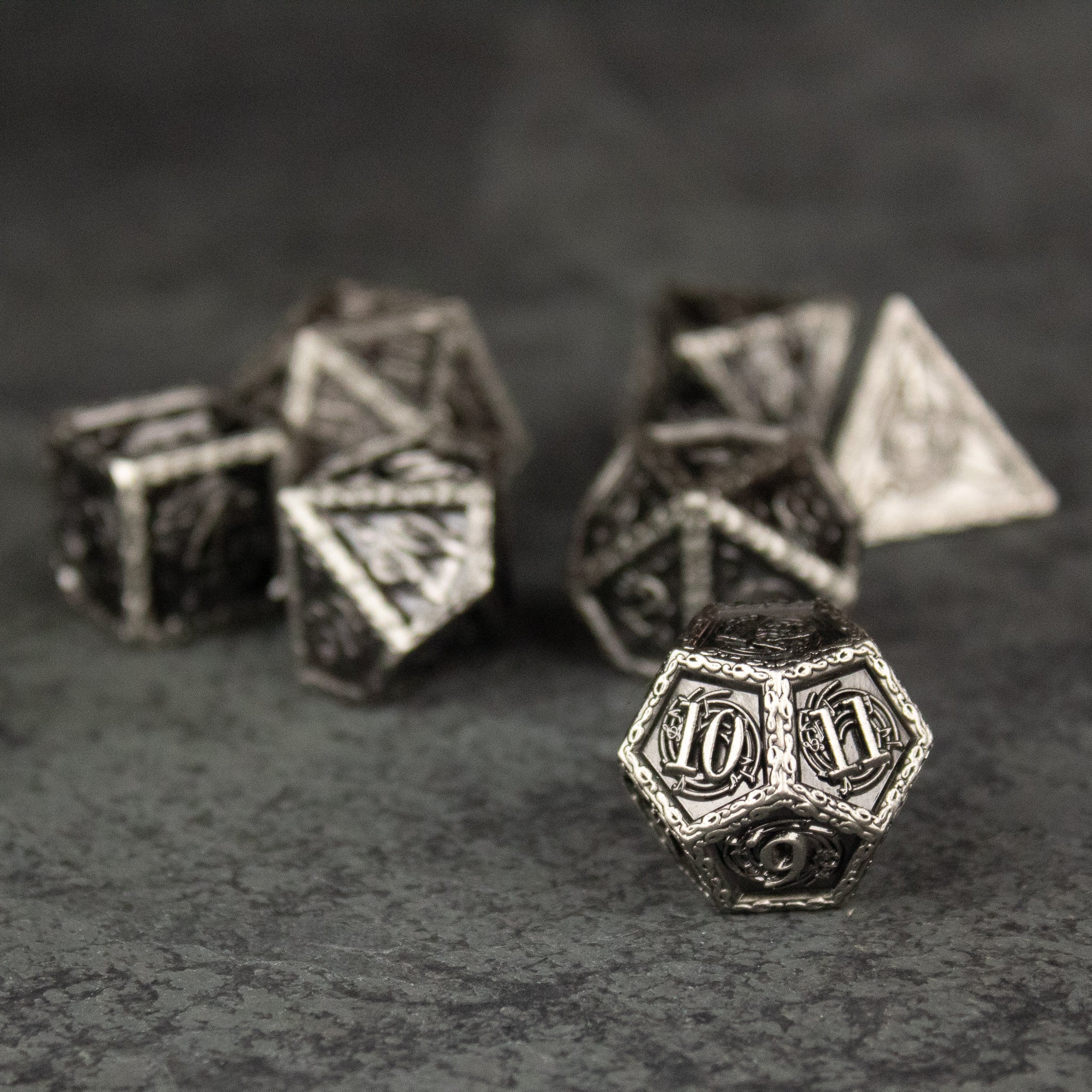 Bardic Inspiration Metal Dice Set - Set of seven silver metal polyhedral dice with intricate engravings and a weathered finish, including d20, d12, d10, d8, d6,