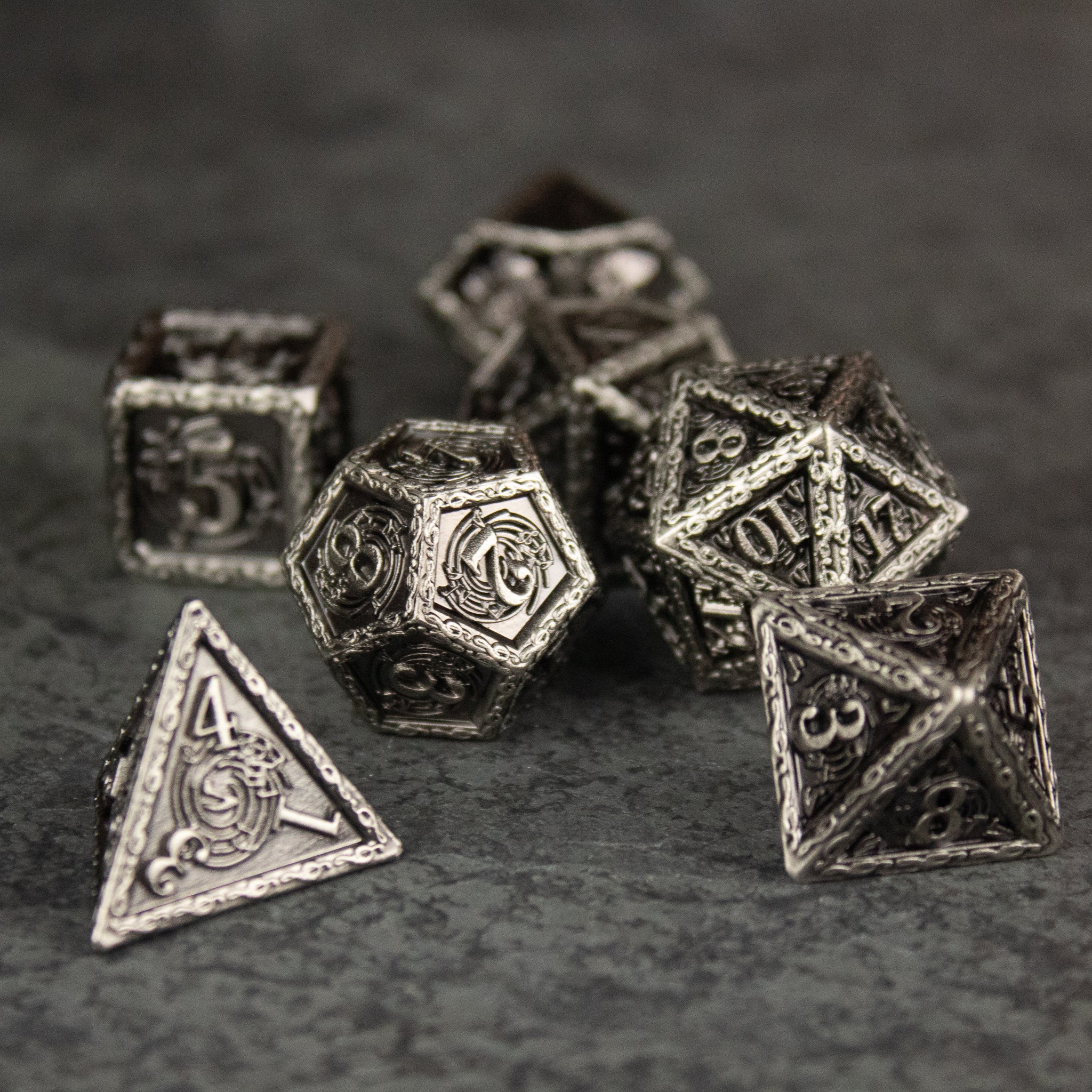 Bardic Inspiration Metal Dice Set - Set of seven metallic RPG dice with engraved numbers and intricate bardic scrollwork designs on each face, finished in.