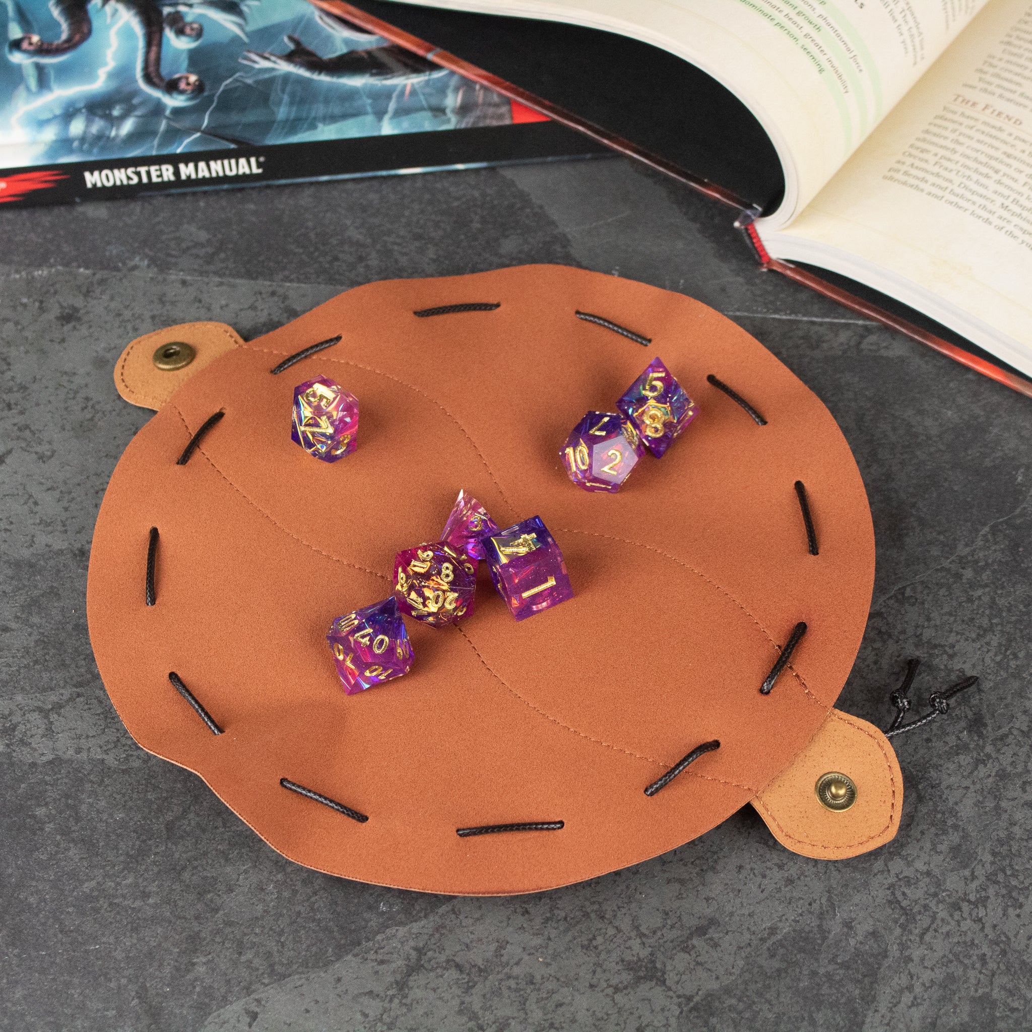 Faux Leather Dice Pouch - Round brown faux leather dice pouch with black lacing and snap closure, holding purple and gold dice.