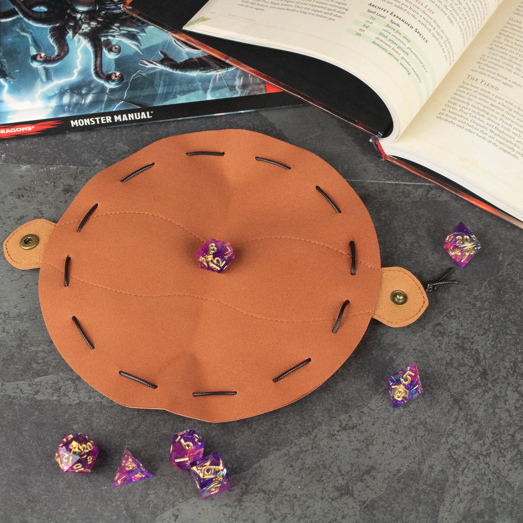 Faux Leather Dice Pouch - Round brown faux leather dice pouch with black stitching and snap button closures, holding purple polyhedral dice.