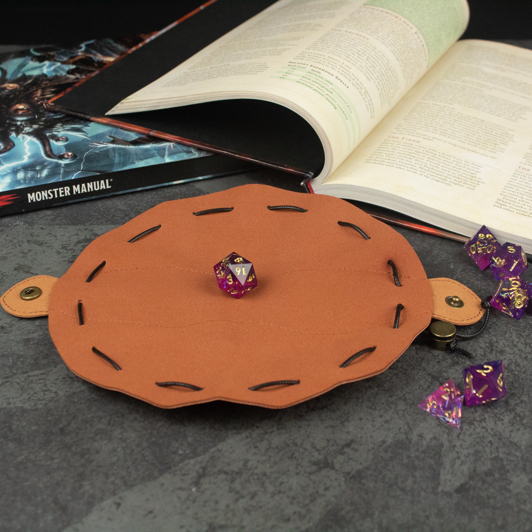 Faux Leather Dice Pouch - Round tan faux leather dice pouch with stitched edges and snap closure, shown open with purple dice inside and nearby gaming